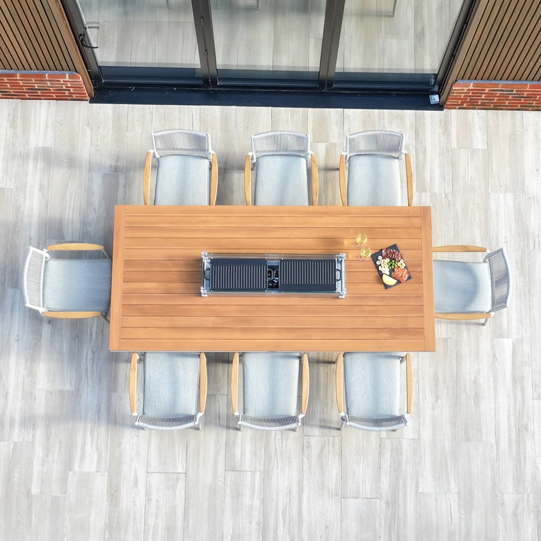 A top view showcases the Tellaro 8 Seat Rectangular Teak Firepit Dining Set in Latte, with wine glasses and a plate of snacks elegantly arranged on the tiled patio.