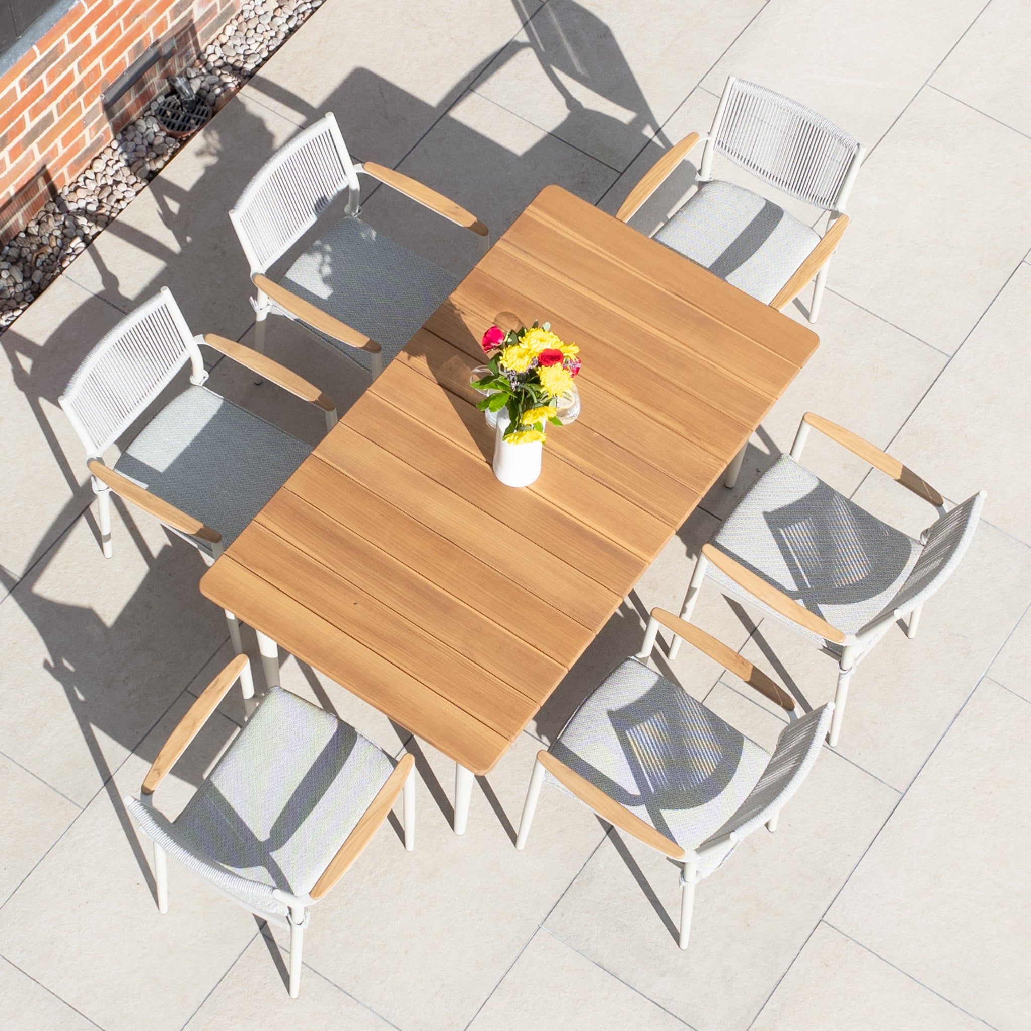 Top view of the Tellaro 6 Seat Rectangular Dining Set with Teak Table in Latte, featuring six white chairs and a colorful flower vase on a tiled surface, ideal for elevating your outdoor living space.