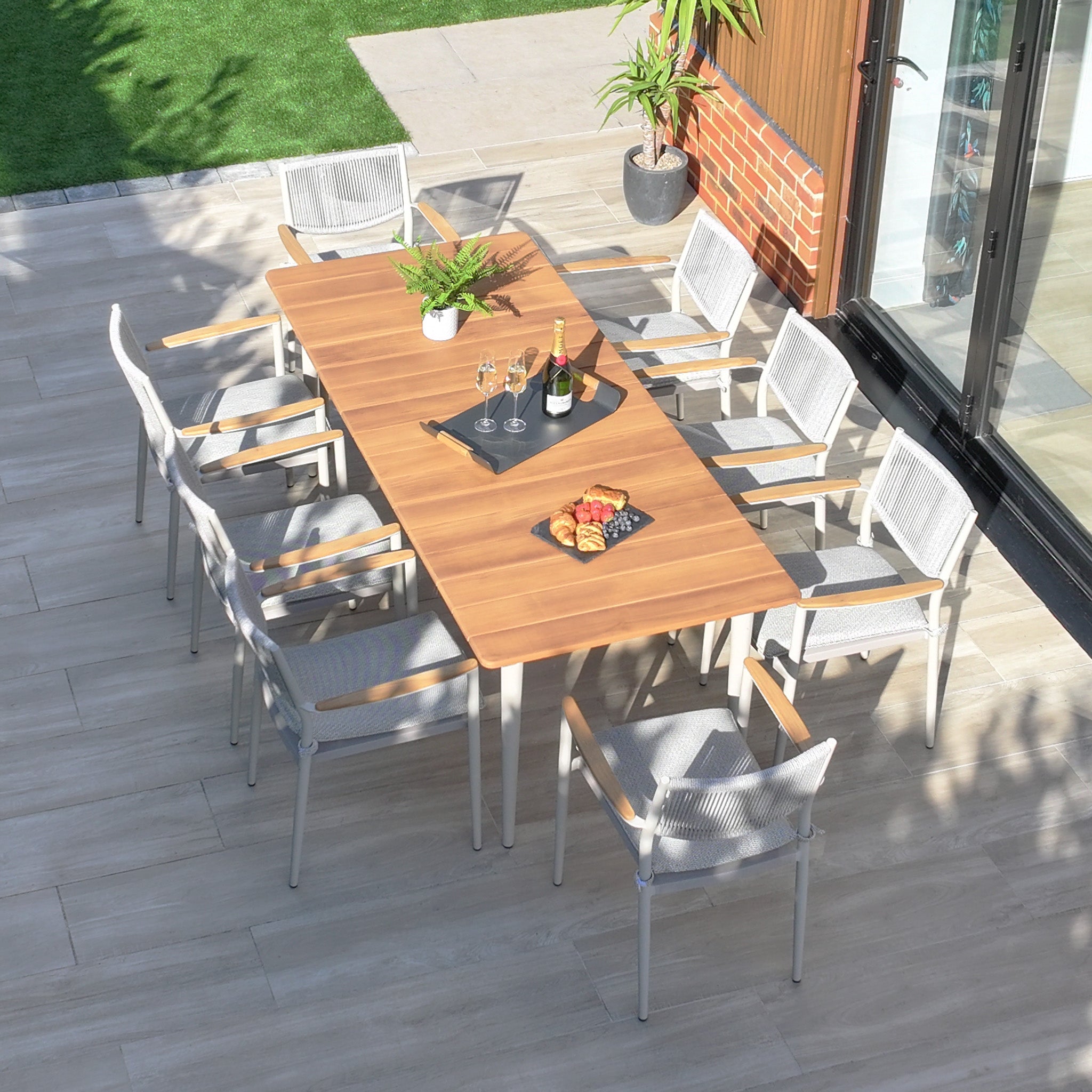 Outdoor patio showcasing the Tellaro 8 Seat Rectangular Dining Set with a weather-resistant teak table in Latte, surrounded by eight chairs, complemented with champagne, glasses, and snacks tray. Perfect for stylish and comfortable outdoor dining.