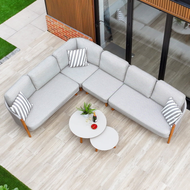 An aerial view of the Merano Large Corner Group Set with Coffee Table in Latte features a gray L-shaped outdoor sofa adorned with striped pillows and round tables on a tiled patio, enhancing the style and functionality of the outdoor living space.