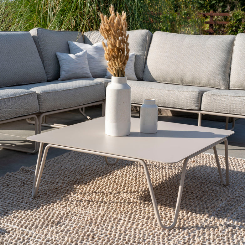 Modern outdoor lounge area featuring a square coffee table, vases, a beige rug, and a gray sectional sofa with hydrophobic rope weave on a patio. The Riviera Luxury Outdoor Corner Group Set in Latte ensures durability with its Rust Proof Tiger Drylac Powder Coating.