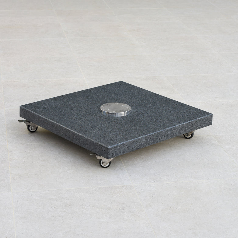 A Granite 120kg Cantilever Parasol Base With Wheels, featuring a large square black platform with a central circular metallic component, is positioned on a tiled floor.