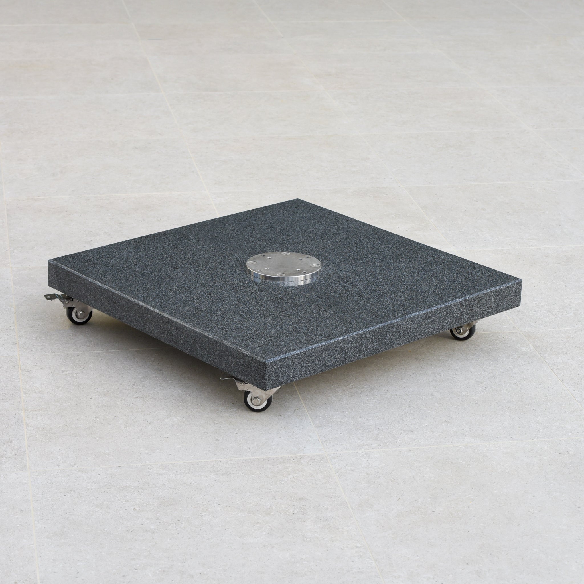 A Granite 90kg Cantilever Parasol Base With Wheels, square and dark grey with a small circular component in the center, resting on a light floor.