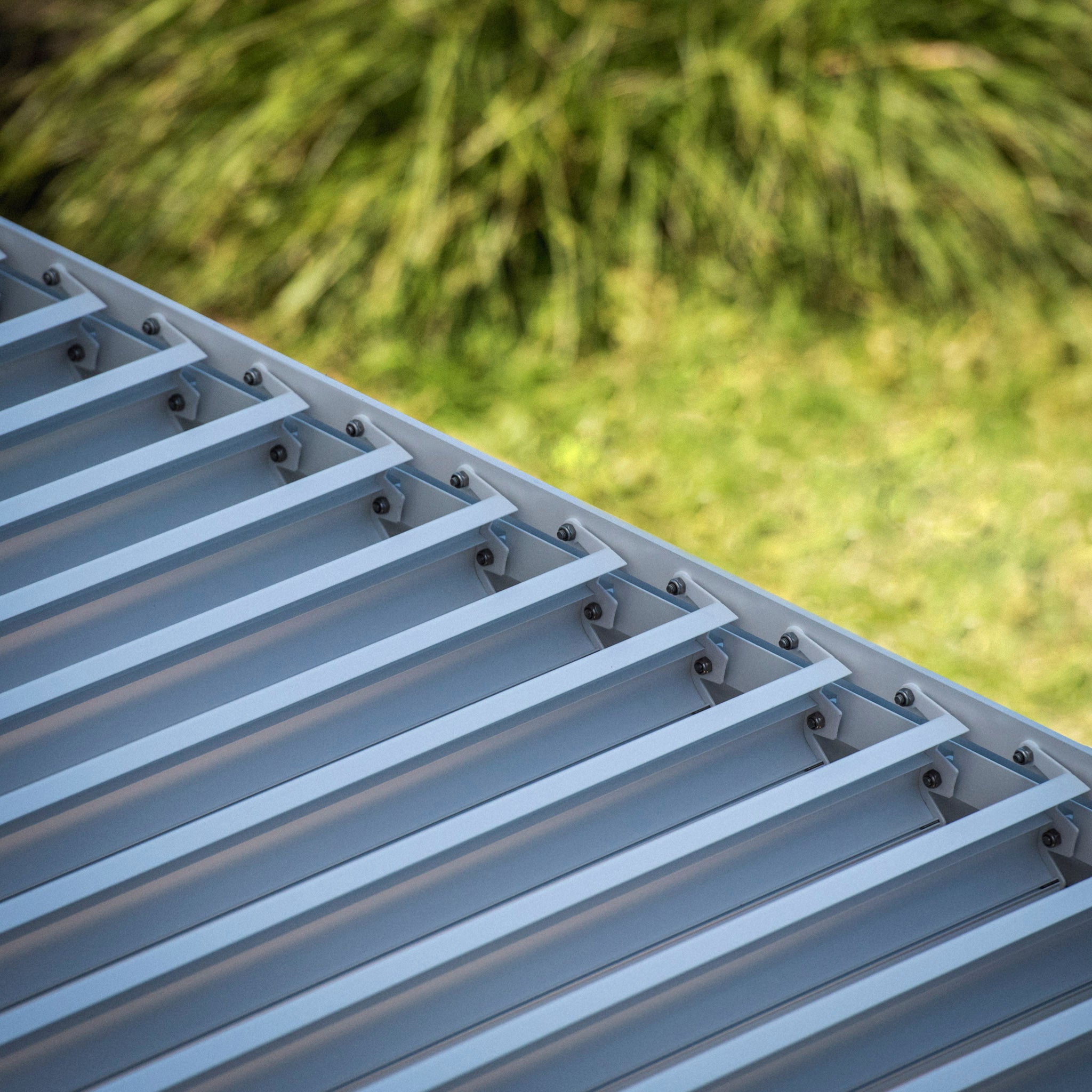 Close-up of a PergoSTET 3m x 3m Square Pergola with 3 Drop Sides and LED Lighting in White, featuring a corrugated metal roof with greenery in the background, showcasing its built-in drainage system that complements modern pergolas.