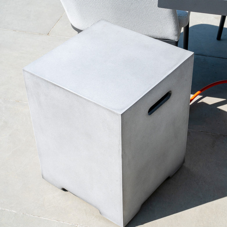 A Stone Grey Ember Gas Storage Box with handles on its sides stands outdoors next to a chair, enhancing the outdoor living space.