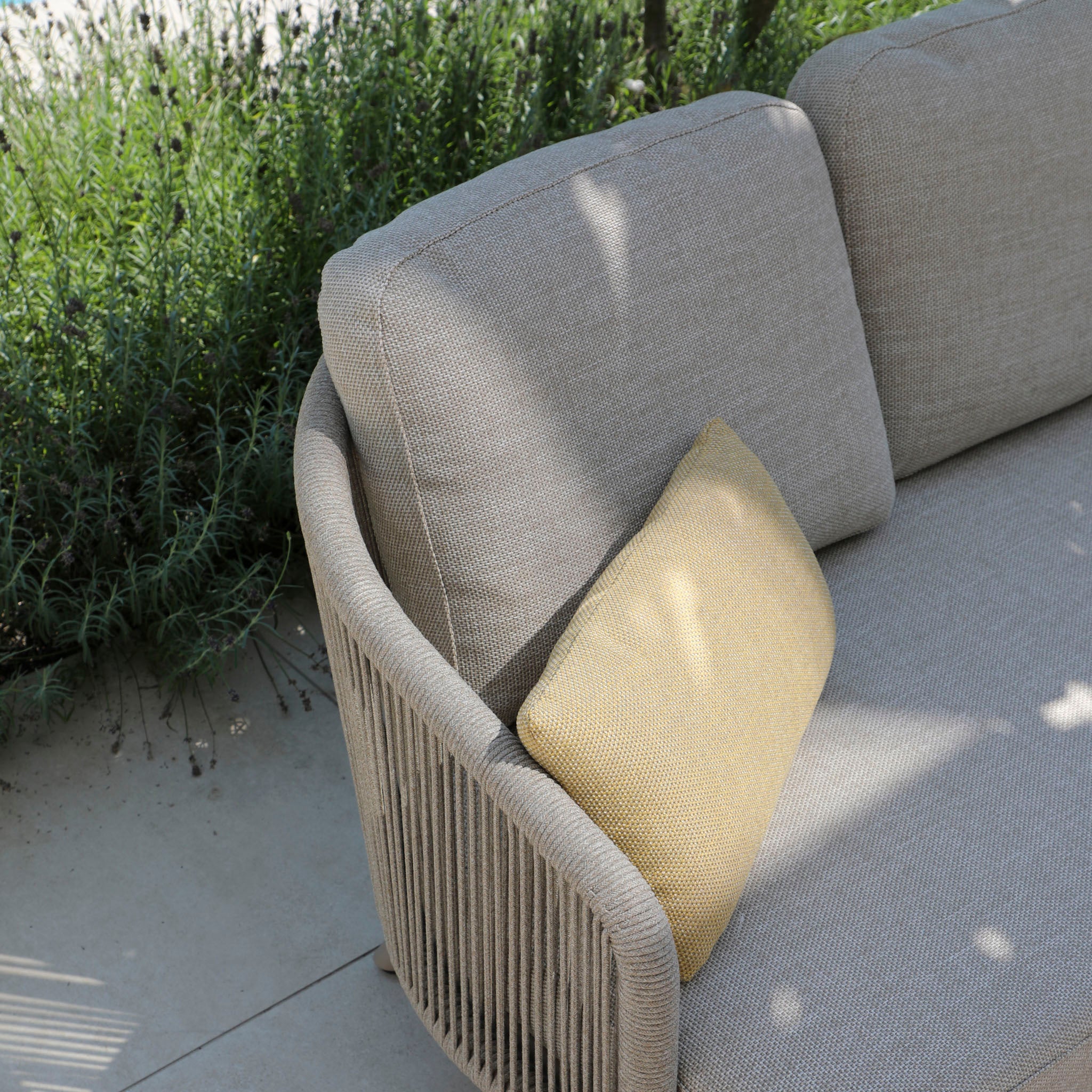 The Dekota 3 Seat Rope Sofa Set, featuring a powder-coated aluminum frame, includes a gray outdoor sofa with a yellow cushion. Nestled on the patio against greenery, dappled sunlight accentuates its hydrophobic olefin rope weave.