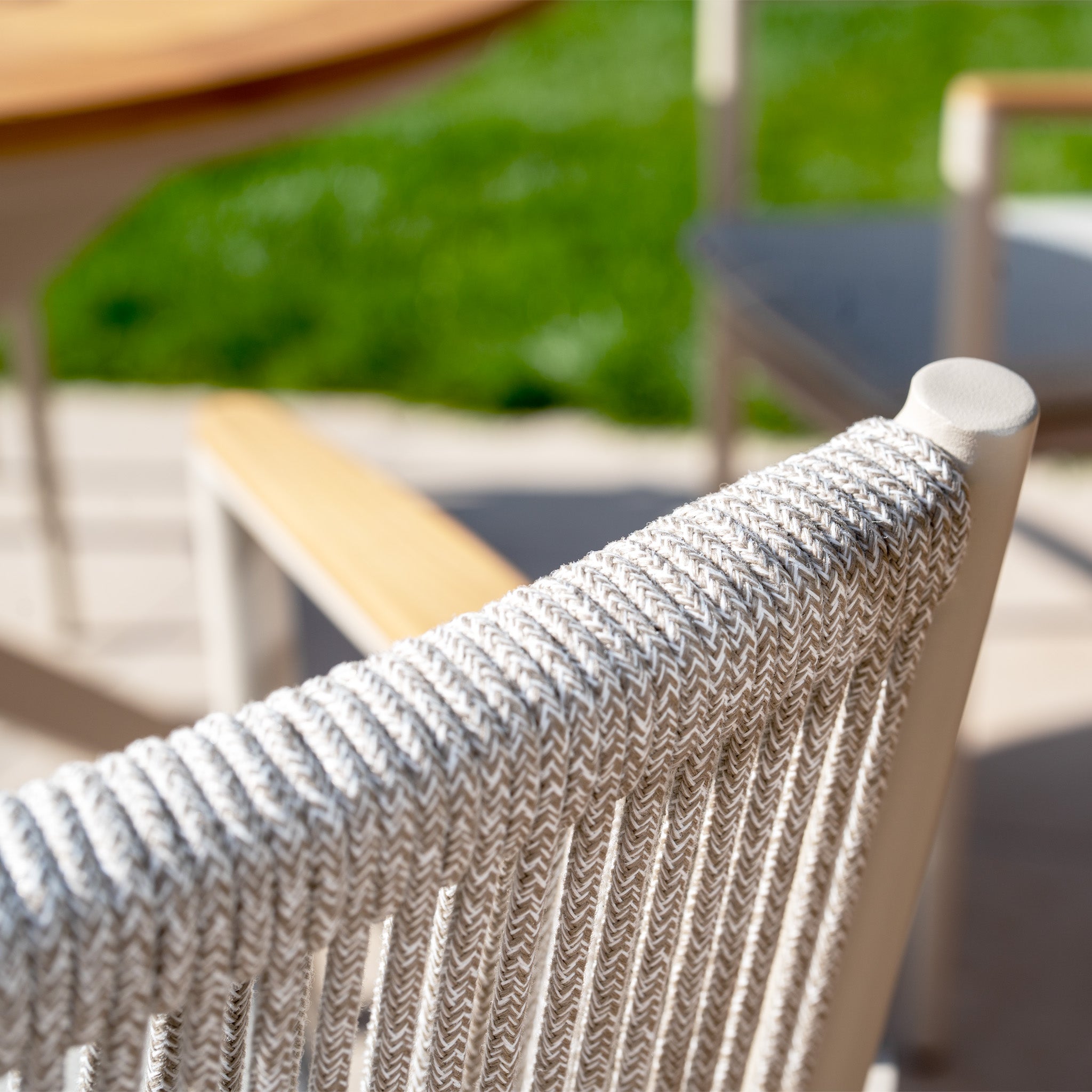 Close-up of a weather-resistant rope chair from the Tellaro 4 Seat Round Dining Set with Teak Table in Latte, with a blurred green grass lawn in the background.