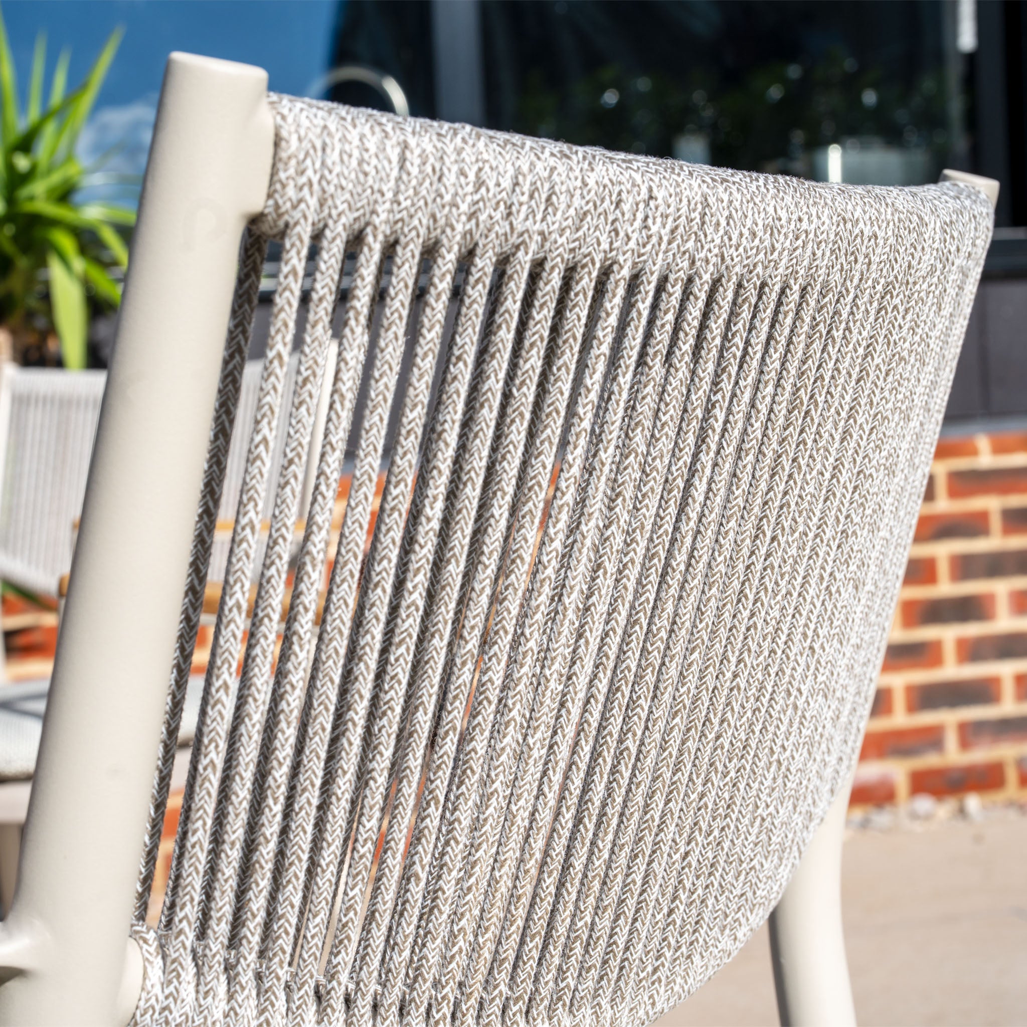 Close-up of the woven, weather-resistant chair back with a metal frame from the Tellaro 4 Seat Round Dining Set with Teak Table in Latte, basking in the sunshine.