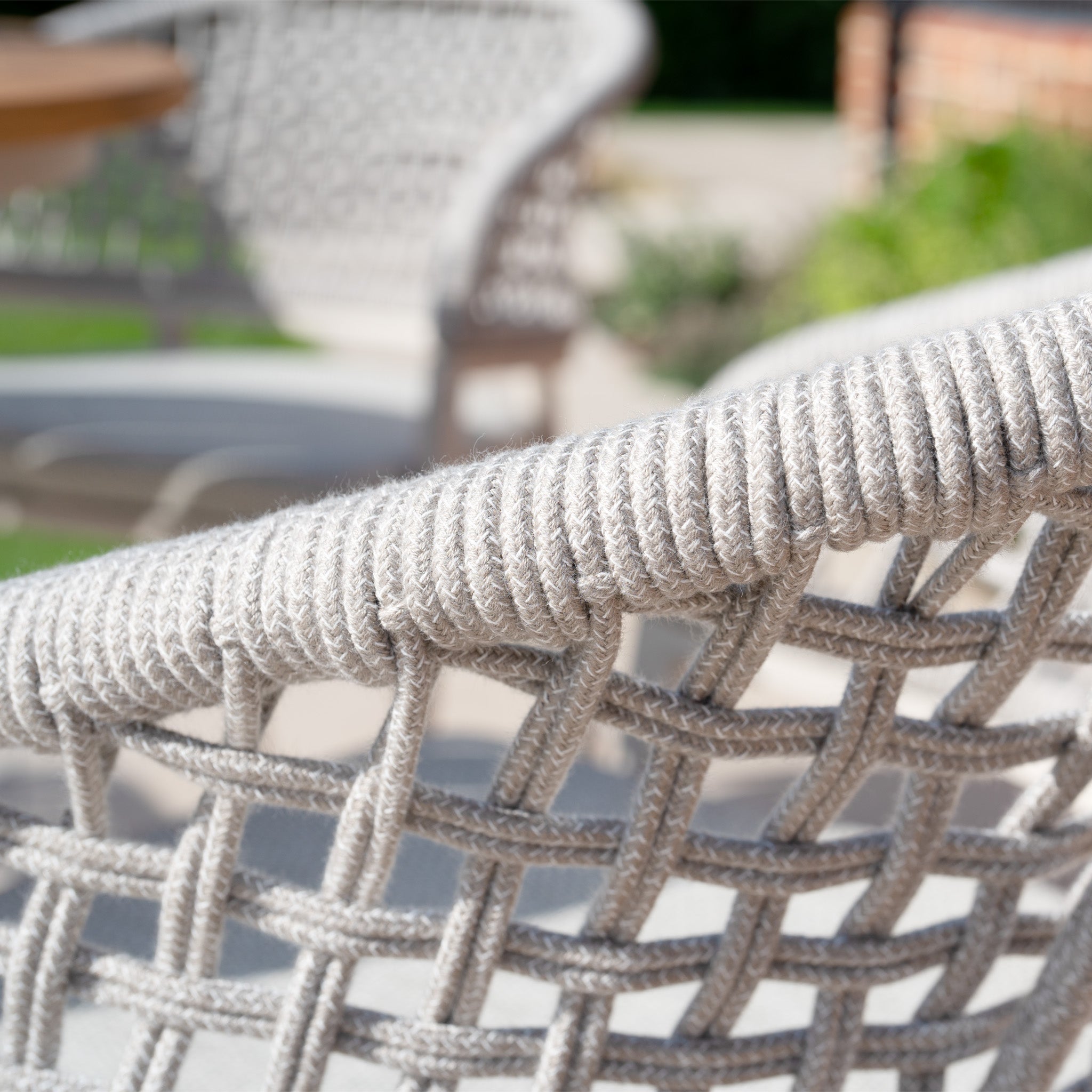 A close-up of the Kalama 4 Seat Round Dining Set with Teak Table in Latte reveals its intricate design, showcasing the woven craftsmanship typical of an elegant outdoor dining set. The teak table's finish adds a touch of natural sophistication.