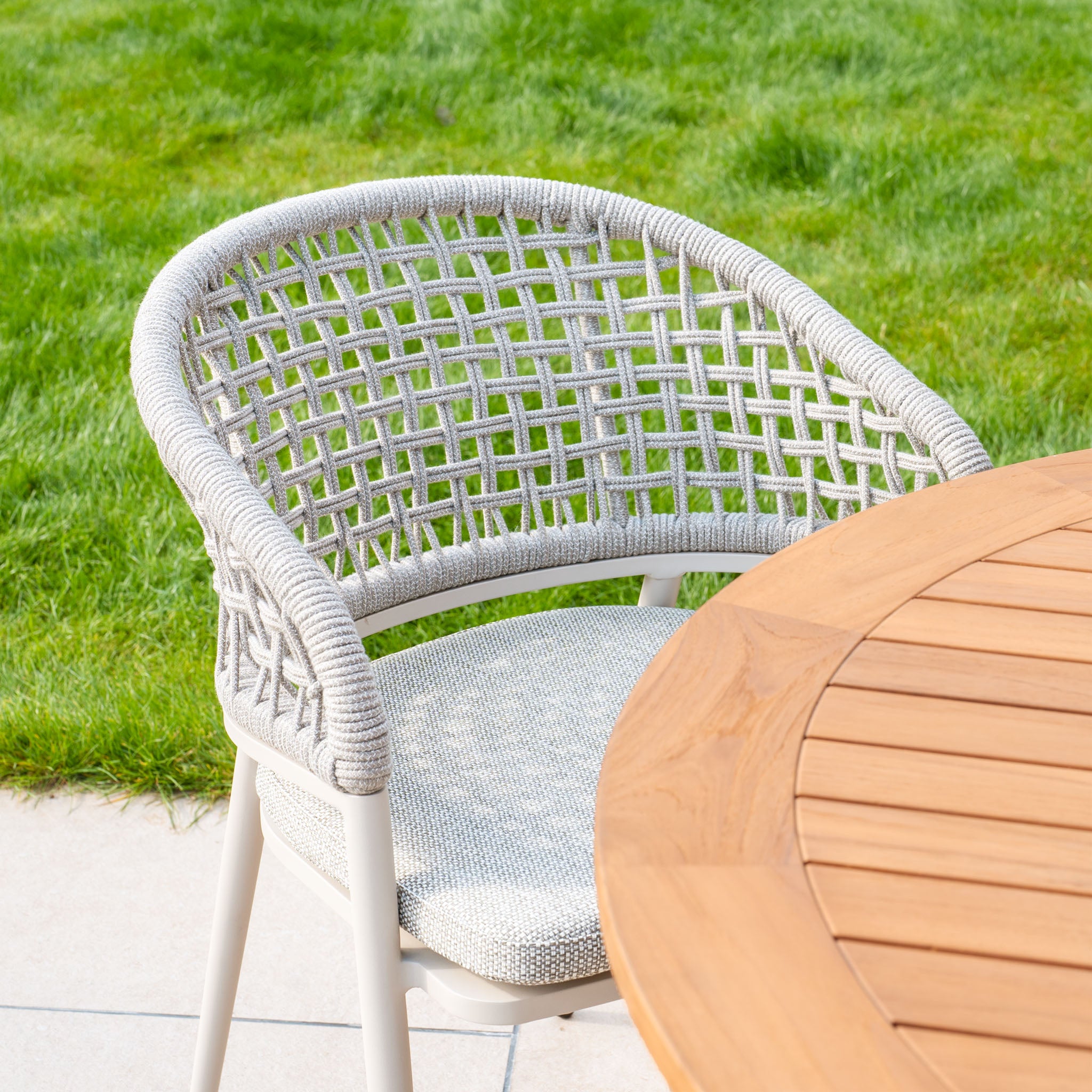 The Kalama 4 Seat Round Dining Set, featuring a teak table in Latte, sits elegantly on a patio surrounded by lush green grass in the background.