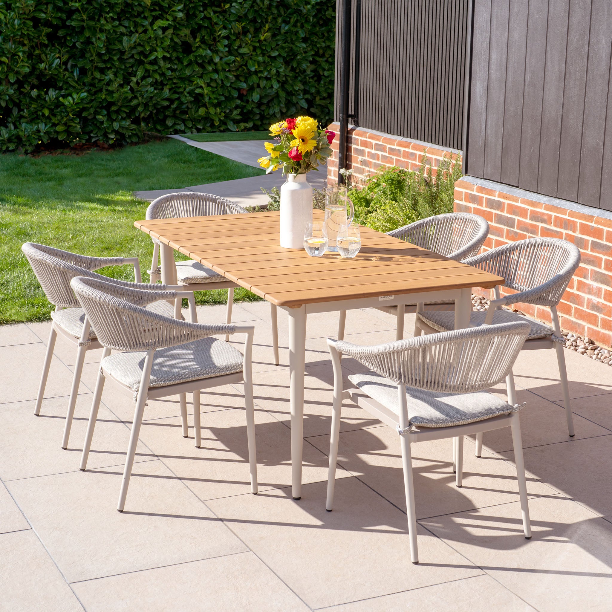 The Cloverly 6 Seat Rectangular Dining Set with a teak table in latte features an elegant aluminium frame and includes six gray chairs. When adorned with flowers and glassware, this patio set turns any sunny garden setting into an inviting oasis.