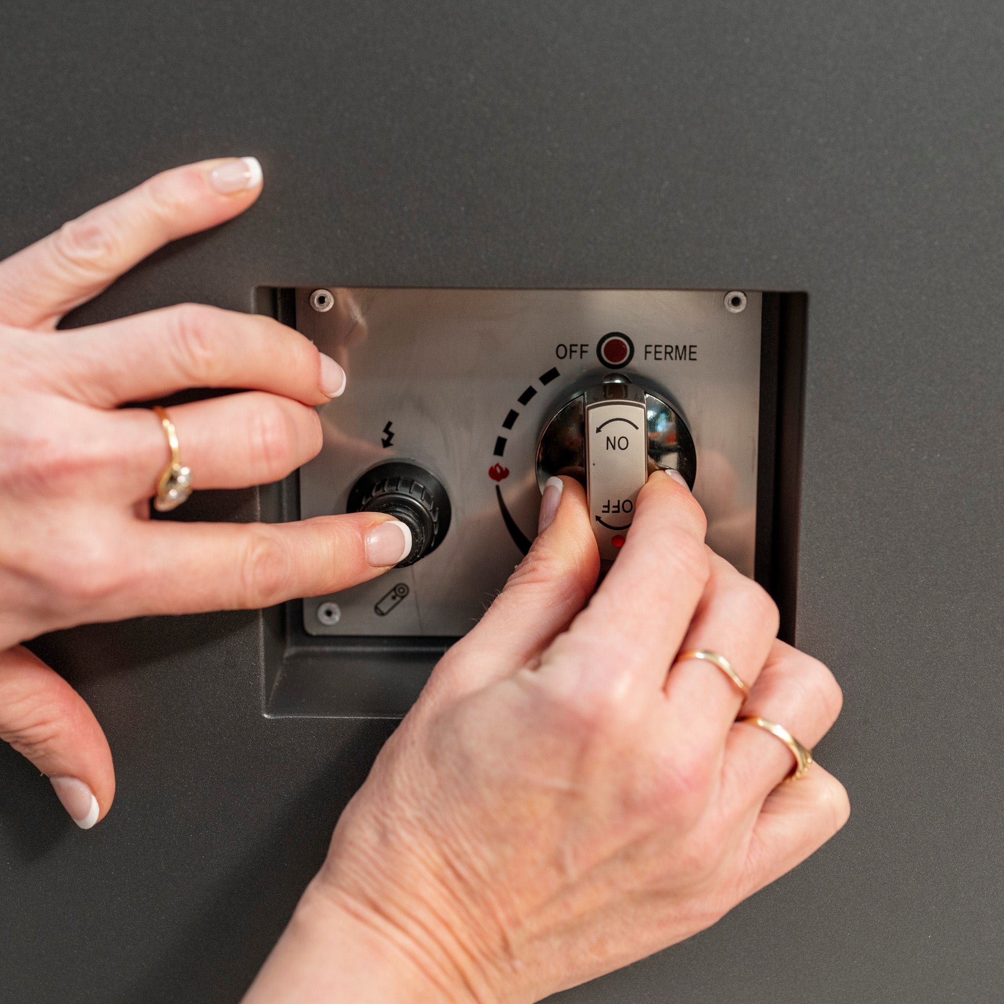 Two hands adjusting controls on an industrial machine panel. One hand is pressing a button, while the other is turning a switch on a Ceramic Firepit Coffee Table in Grey.