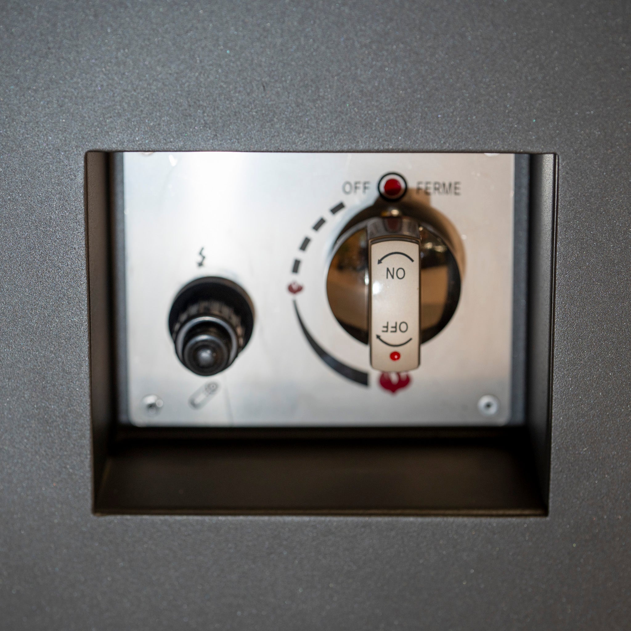 Close-up of a control panel with an ON/OFF switch and various black knobs and indicators against the grey surface of the Ceramic Firepit Coffee Table, featuring a sleek Aluminium Frame.