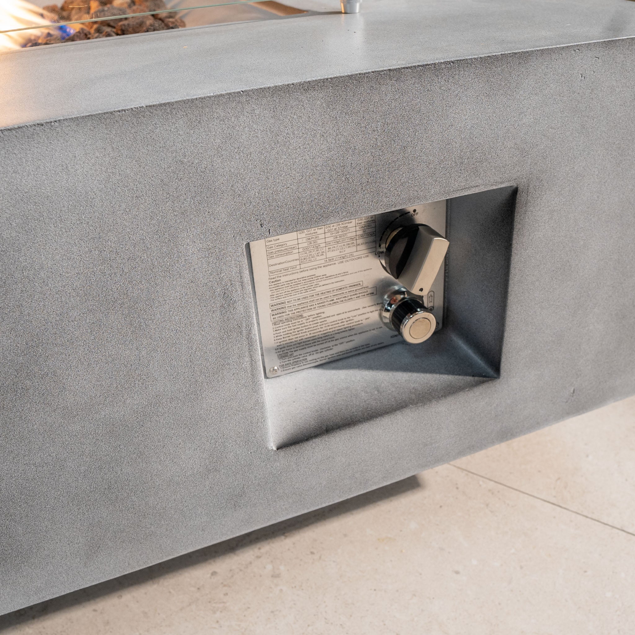 Close-up of a control panel on a Stone Grey Ember Rectangular Firepit Coffee Table, featuring a dial and an instructional label, all housed in durable 304 stainless steel.