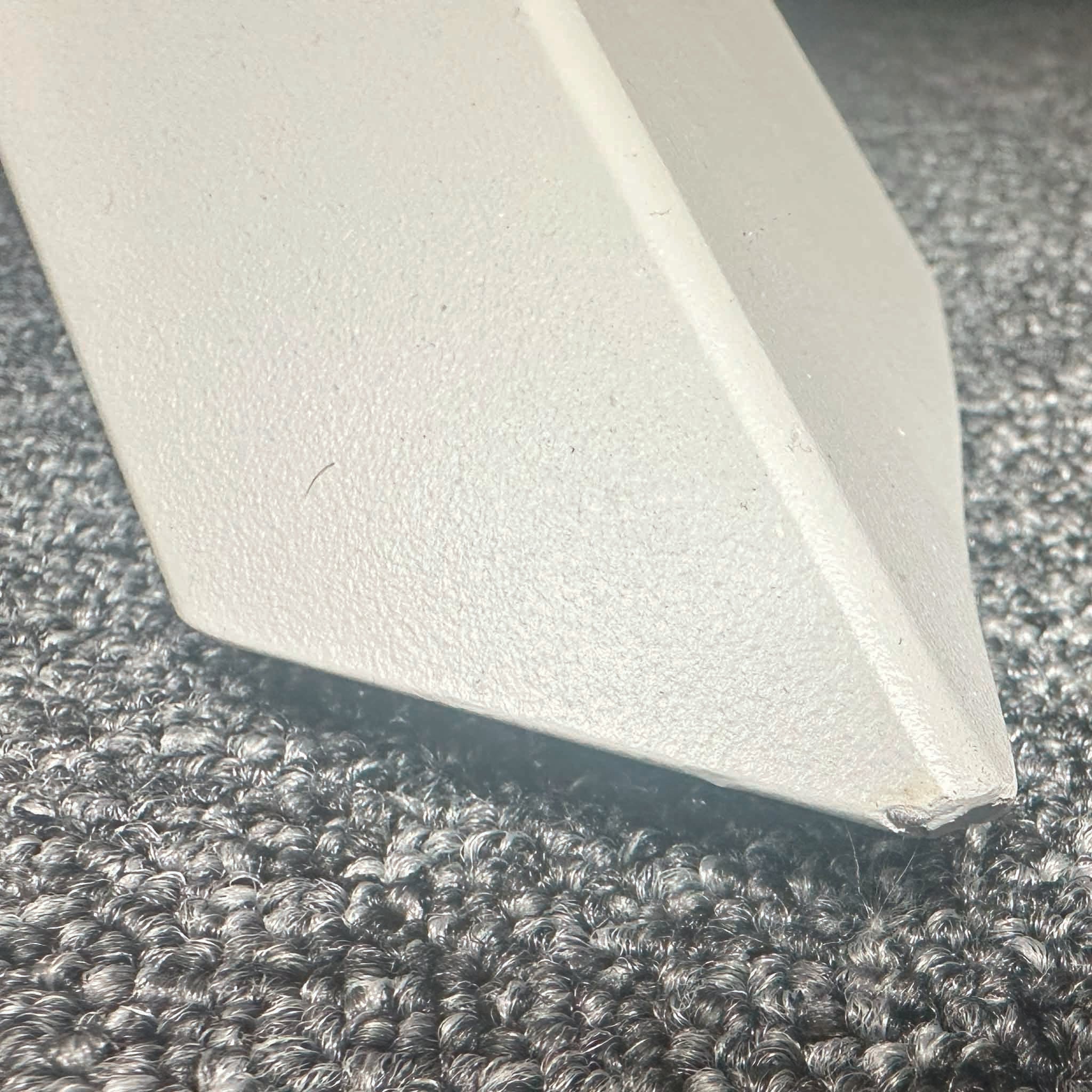 Close-up of a pointed metal object from the Bernini 6 Seat Round Dining with Teak Table in Light Grey (Ex Display) resting on a textured carpet floor.