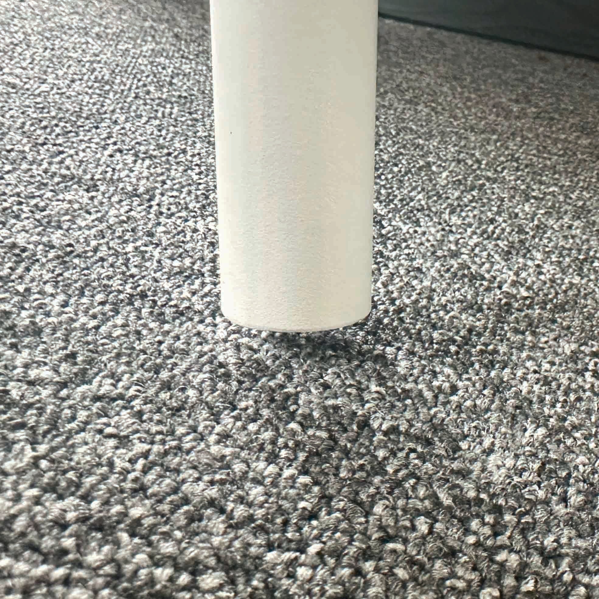 Close-up of a white table leg from the Bernini 6 Seat Round Dining with Teak Table in Light Grey (Ex Display) on a grey carpeted floor.