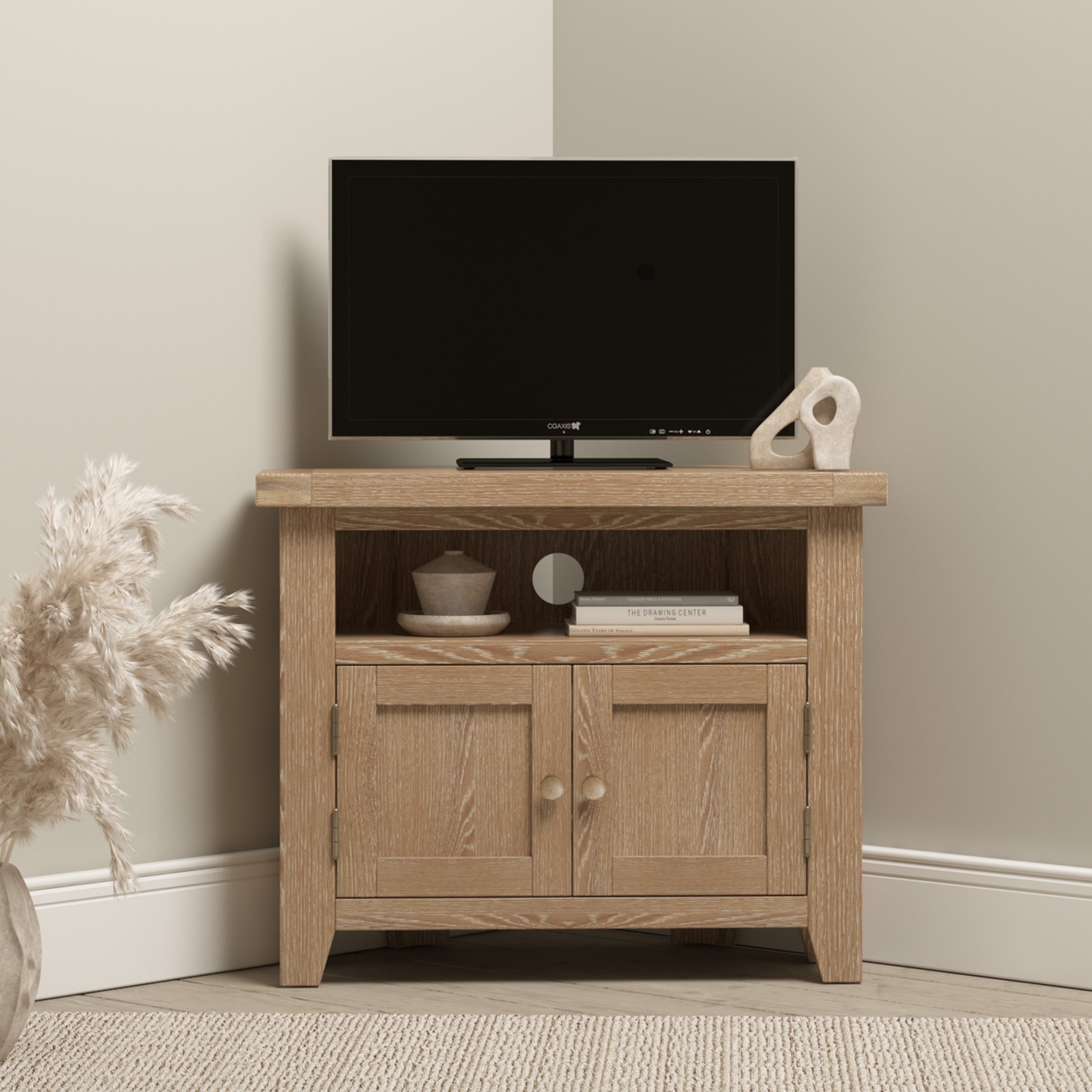 A compact TV on the Burford Corner Media Unit in Natural Oak, featuring decorative items, situated in the corner of a neutrally-toned room with a plant, enhancing the space with its natural oak finish and rustic appeal.