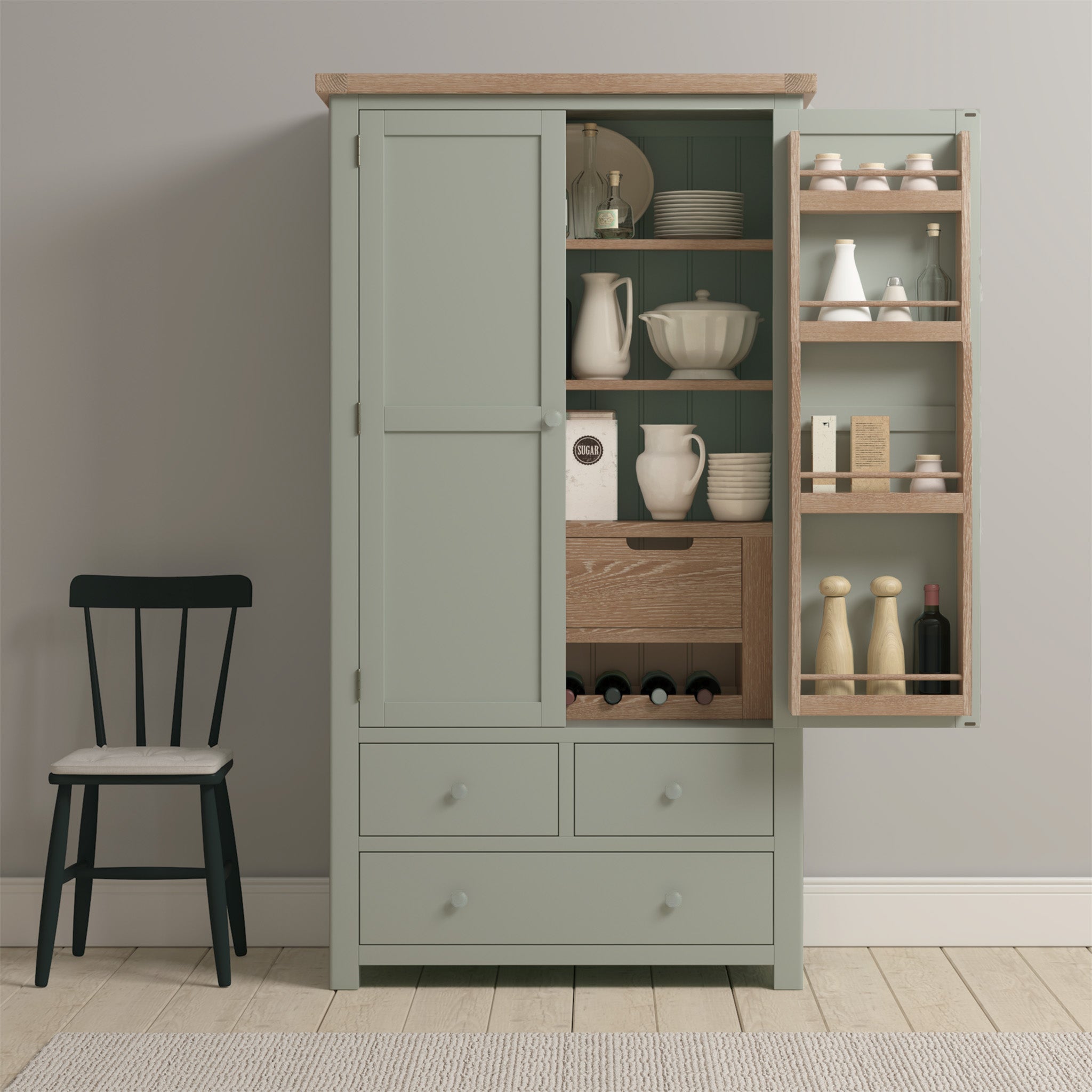 The Burford Double Larder Unit in Sage Green features an open door displaying shelves filled with dishes and spices. It stands elegantly next to a black chair on a cozy rug, adding a touch of natural oak warmth to the kitchen's ambiance.