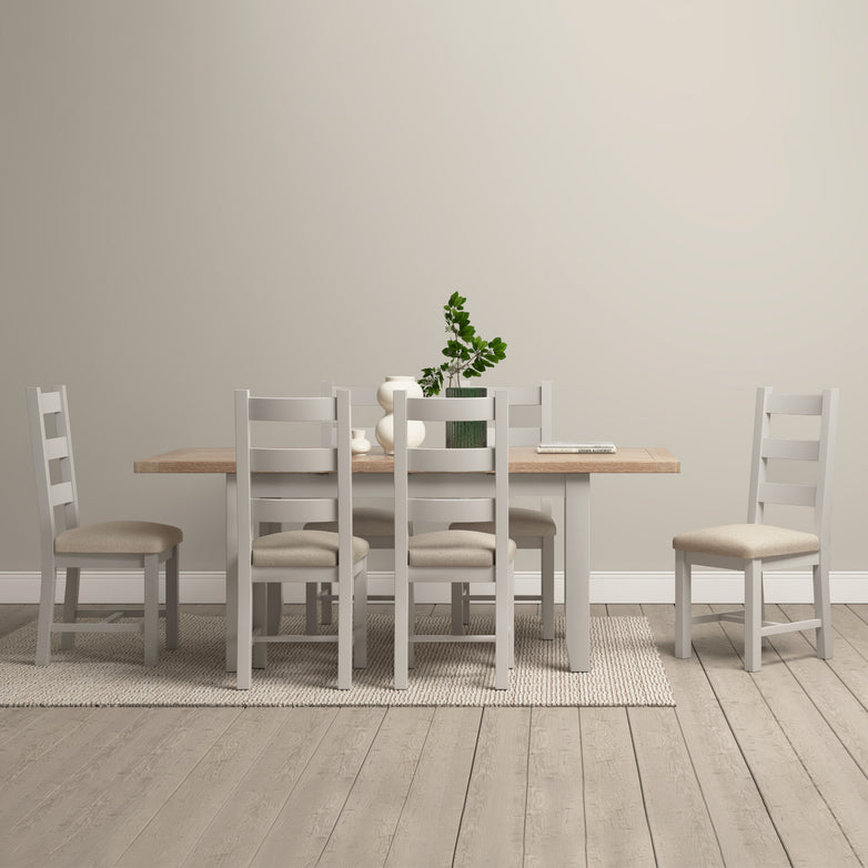 Minimalist dining room showcasing an elegant Burford 4-6 Seater Extending Dining Table in pebble grey, accompanied by six chairs and a potted plant centerpiece on a light-colored rug.