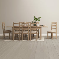 A dining room featuring the Burford 6-10 Seater Extending Dining Table in natural oak, surrounded by eight chairs, with a green plant centerpiece and light-colored walls and floor.