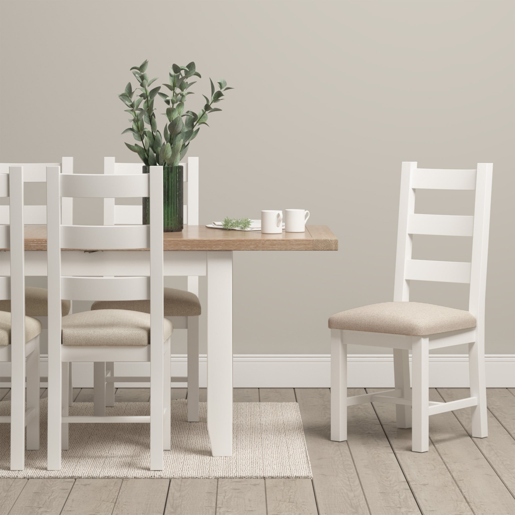 A contemporary dining room showcases the Burford 6-10 Seater Extending Dining Table in Warm White, paired with sleek white chairs. The arrangement is enhanced by a vase with a plant and two cups, highlighting the exceptional craftsmanship of the furniture.