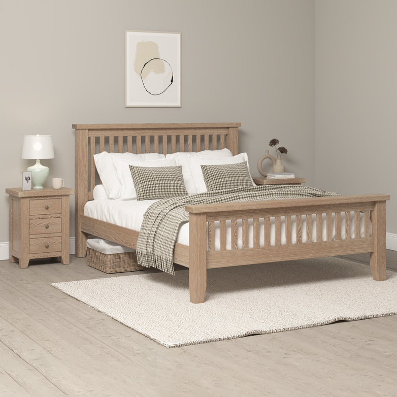 Cozy bedroom featuring a Burford 5ft High-End Kingsize Bed Frame in natural oak, complemented by white bedding, a bedside table with a lamp, and abstract art on the beige wall, creating an upscale ambiance.