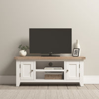 A minimalist living room showcases a Burford 120cm Media Unit in Warm White, elegantly supporting the TV. The area is tastefully adorned with plants and a vase, adding rustic charm to the serene setting.