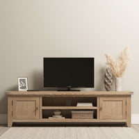 The Burford Large 180cm Media Unit in Natural Oak adds a rustic touch, holding a TV, framed photo, and decorative vase with pampas grass. A basket nestles underneath for extra charm.