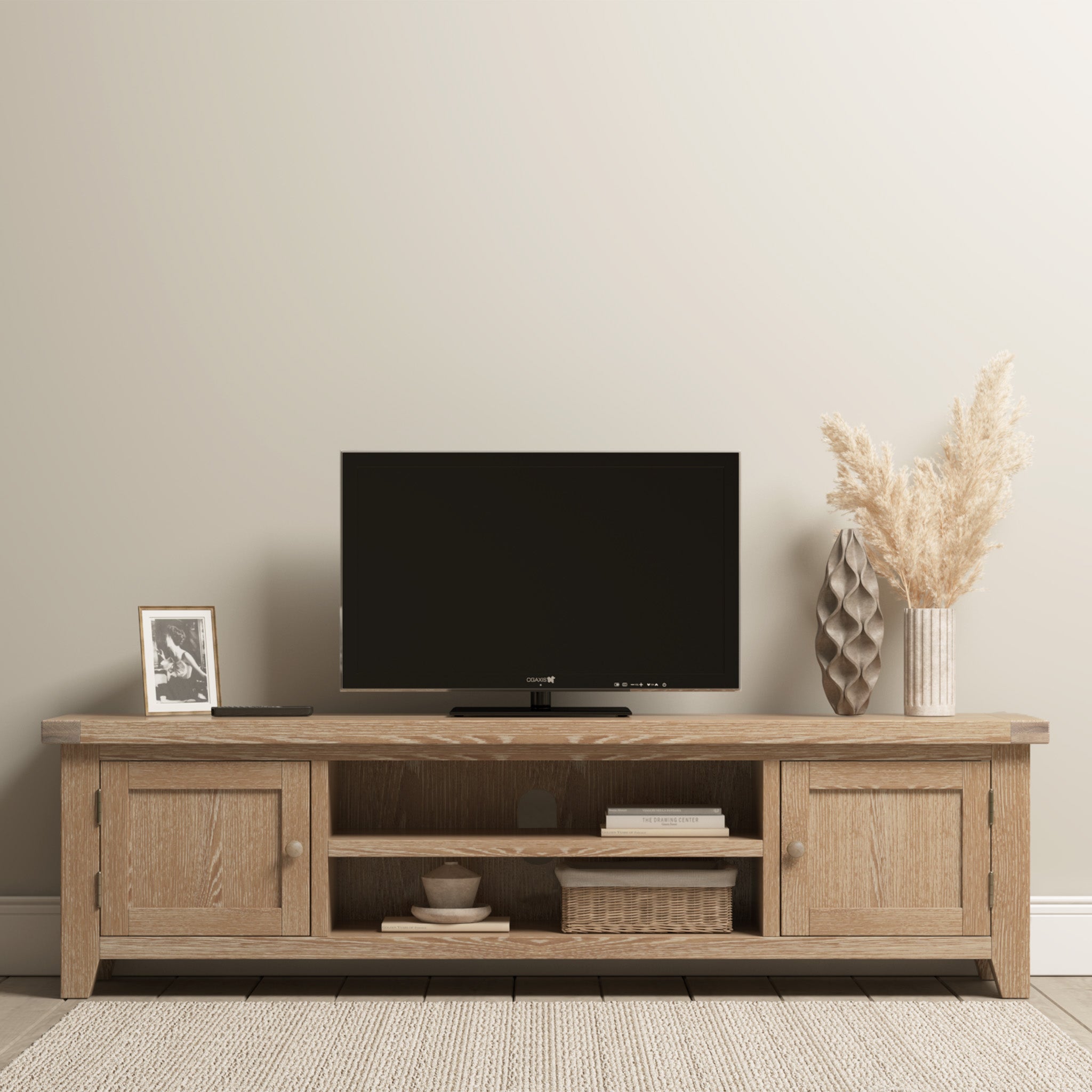 The Burford Large 180cm Media Unit in Natural Oak holds a flat-screen TV, photo frame, vase of pampas grass, and basket in a neutral living room with sleek cable management for tidiness.