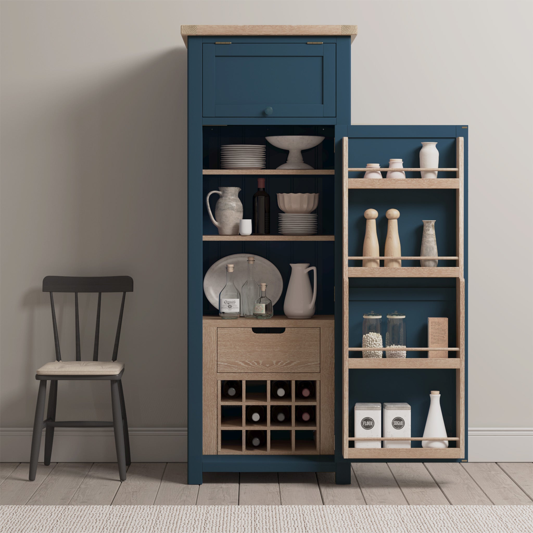 The Burford Single Larder Unit in Navy Blue, with doors open to showcase generous kitchen storage and wine racks, stands tall. A dark wooden chair crafted from natural oak sits invitingly on the left.