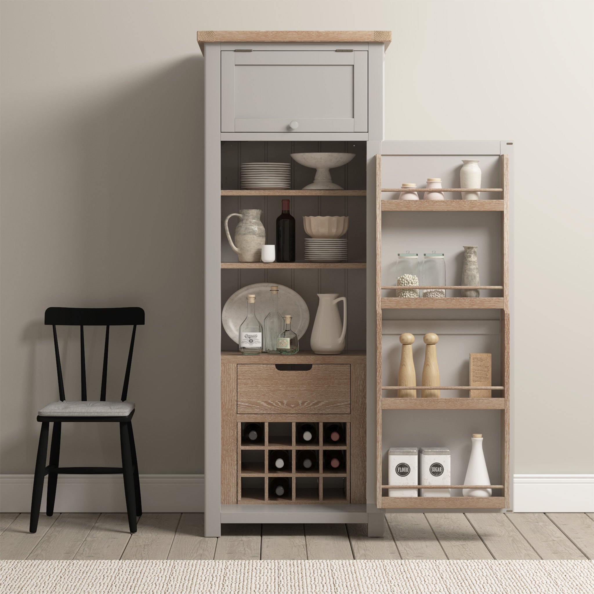 The Burford Single Larder Unit in Pebble Grey, containing dishes, a wine rack, and condiments, demonstrates optimal kitchen storage. A black chair is positioned to the left against a neutral wall and rug, accentuating the natural oak tones of the larder unit.