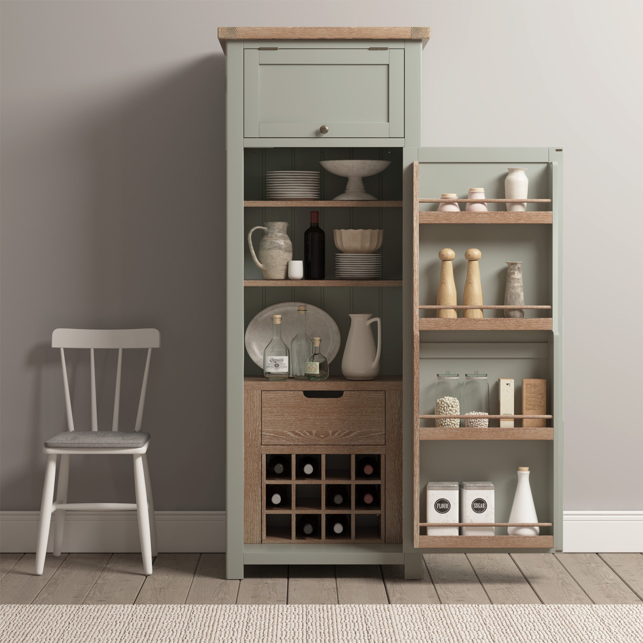 The Burford Single Larder Unit in Sage Green features an open door showcasing shelves filled with dishes, bottles, a wine rack, and spices, providing ample kitchen storage. A chair is placed nearby.