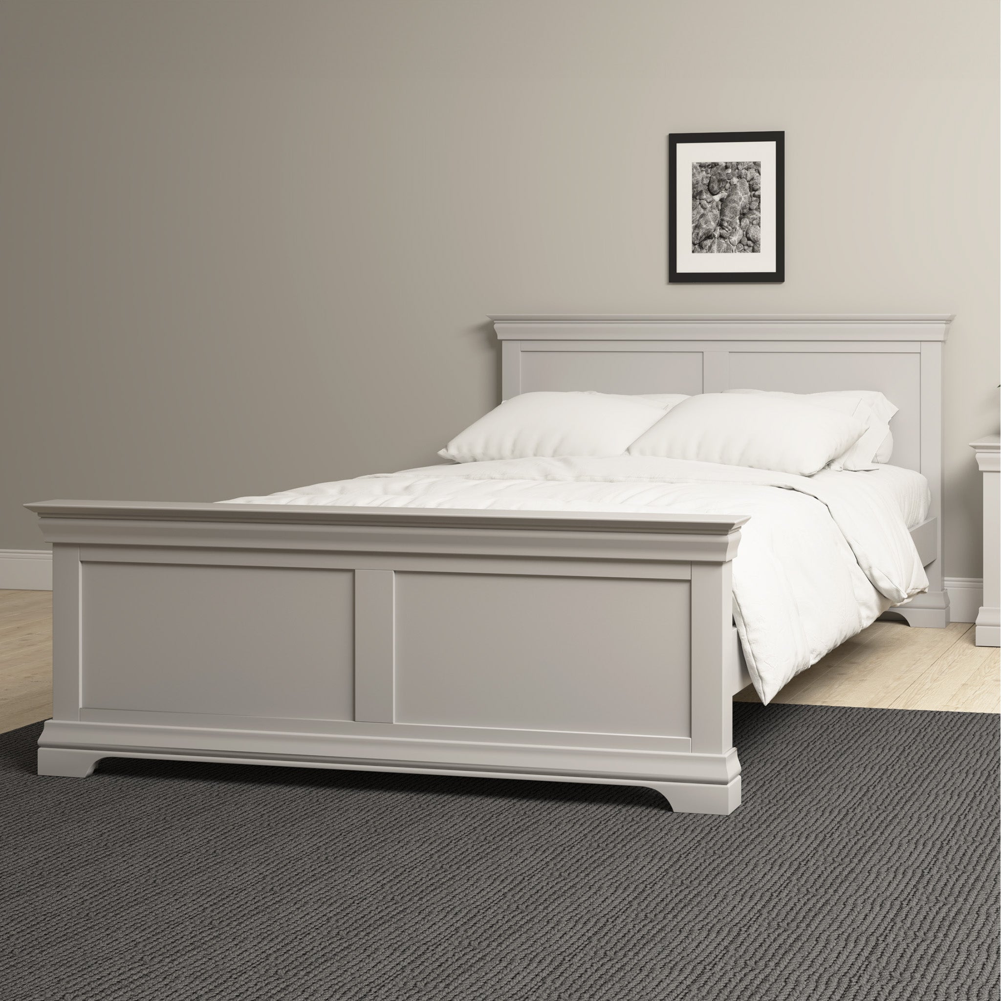 The Chalbury 5ft High-End Kingsize Bed Frame in Pebble Grey, paired with white bedding in a gray-painted room, features a framed picture and dark carpet, epitomizing contemporary design and premium craftsmanship.