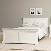 Warm white Chalbury 4ft 6" high-end double bed frame with striped pillows in a bedroom featuring two black-and-white photos on the wall and a light rug on the floor.