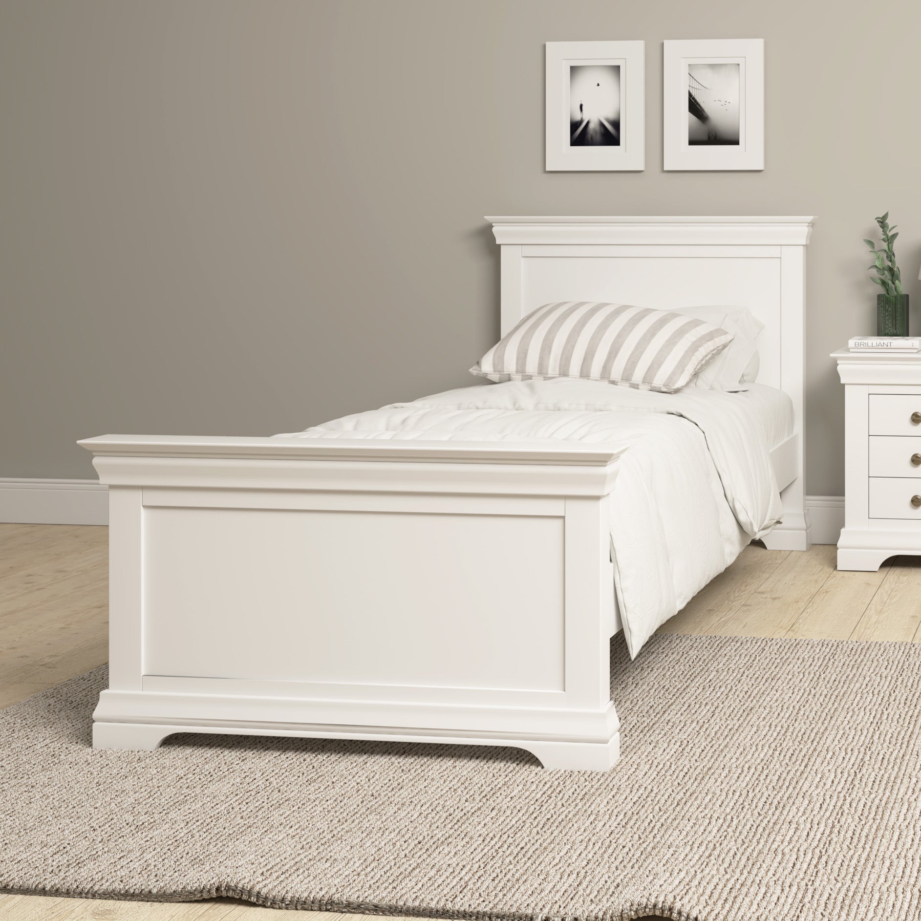 The Chalbury 3ft High-End Single Bed Frame in warm white pairs beautifully with the solid oak floor, showcasing a white bed accented with striped pillows and beige bedding. Above, two framed pictures enhance the cozy ambiance of the space against beige walls and a plush rug.