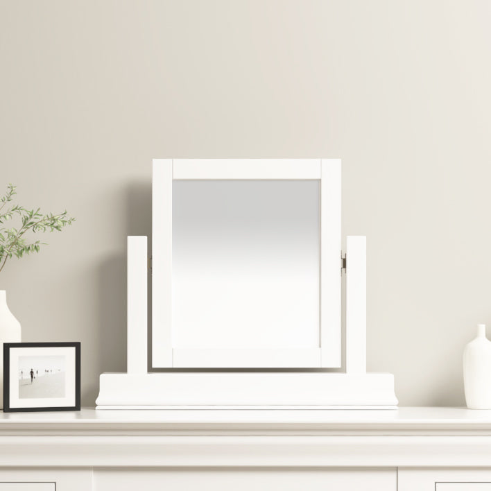 The Chalbury Mirror in Warm White, featuring a contemporary design, rests gracefully on a light-colored dresser with its warm white frame. A small vase and framed photo provide charming accents to the serene setting.