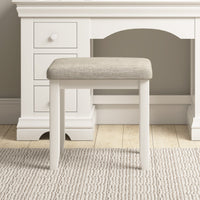 A Chalbury Stool in Warm White, featuring a beige built-in cushion, sits elegantly in front of a vanity table.