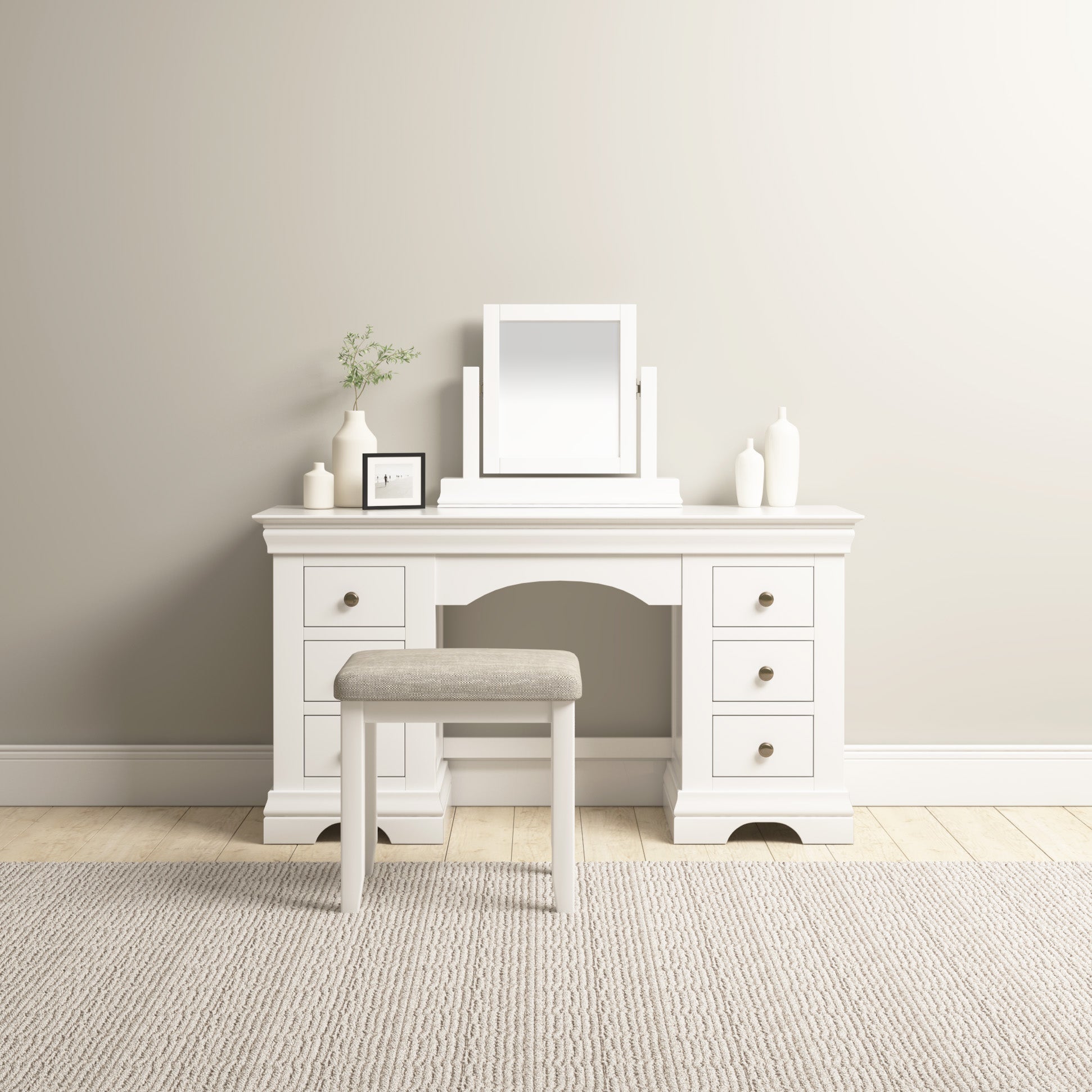 A white vanity table with a Chalbury Mirror in Warm White, six drawers, and a cushioned stool rests on a beige rug in a minimalistic room, highlighting contemporary design.