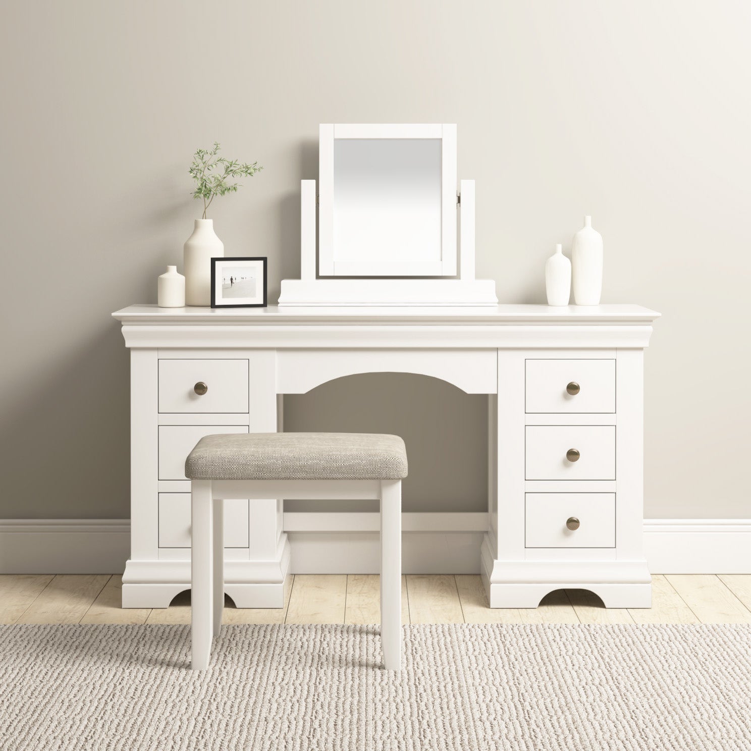 The Chalbury Dressing Table with Drawers in Warm White has six drawers, adorned with small plants and framed photos on top, and comes with a cushioned bench.