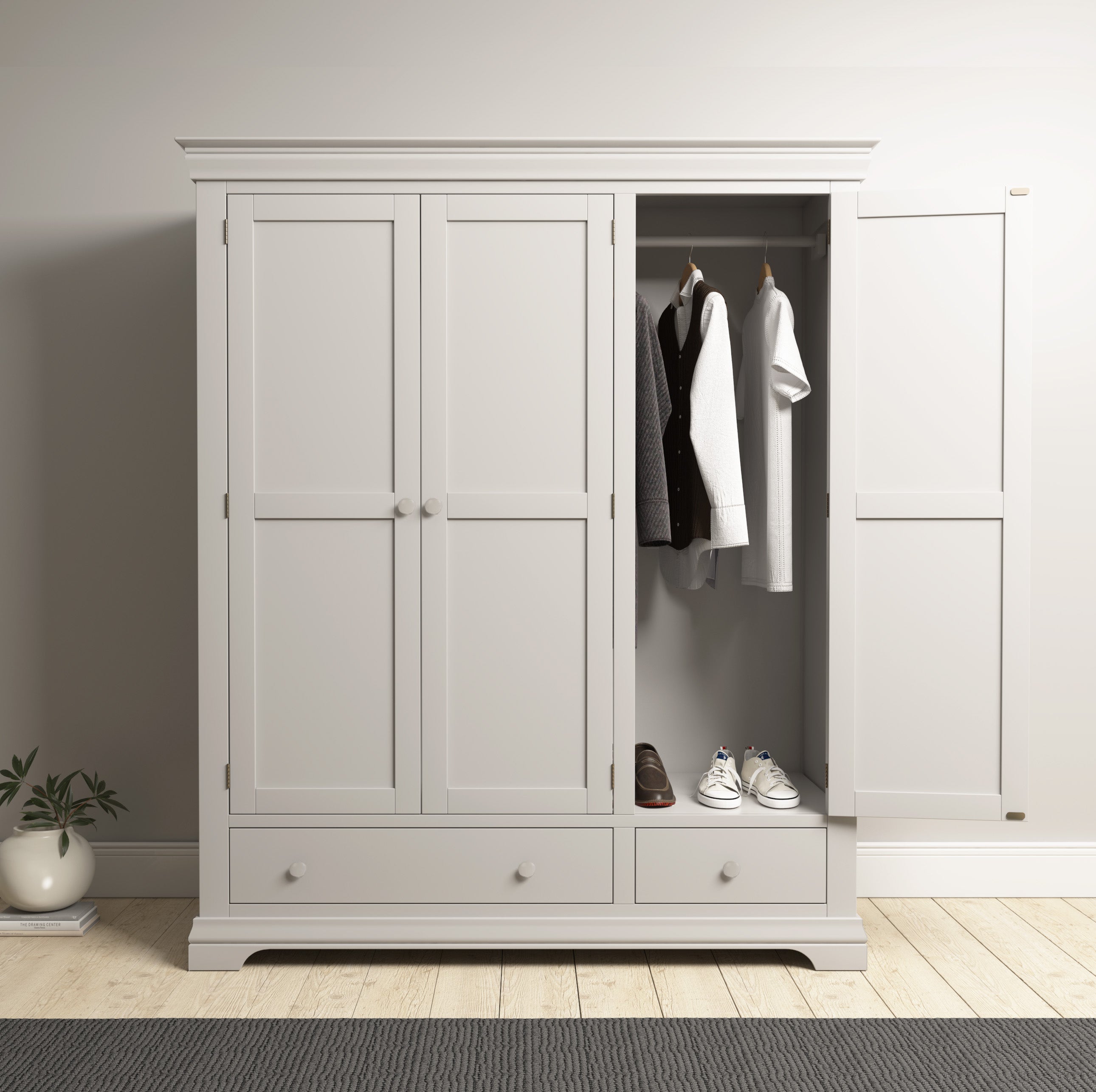 The Chalbury Triple Wardrobe in Pebble Grey, organized with clothes and shoes inside, sits open in your bedroom and perfectly complements the light walls and wooden floors.