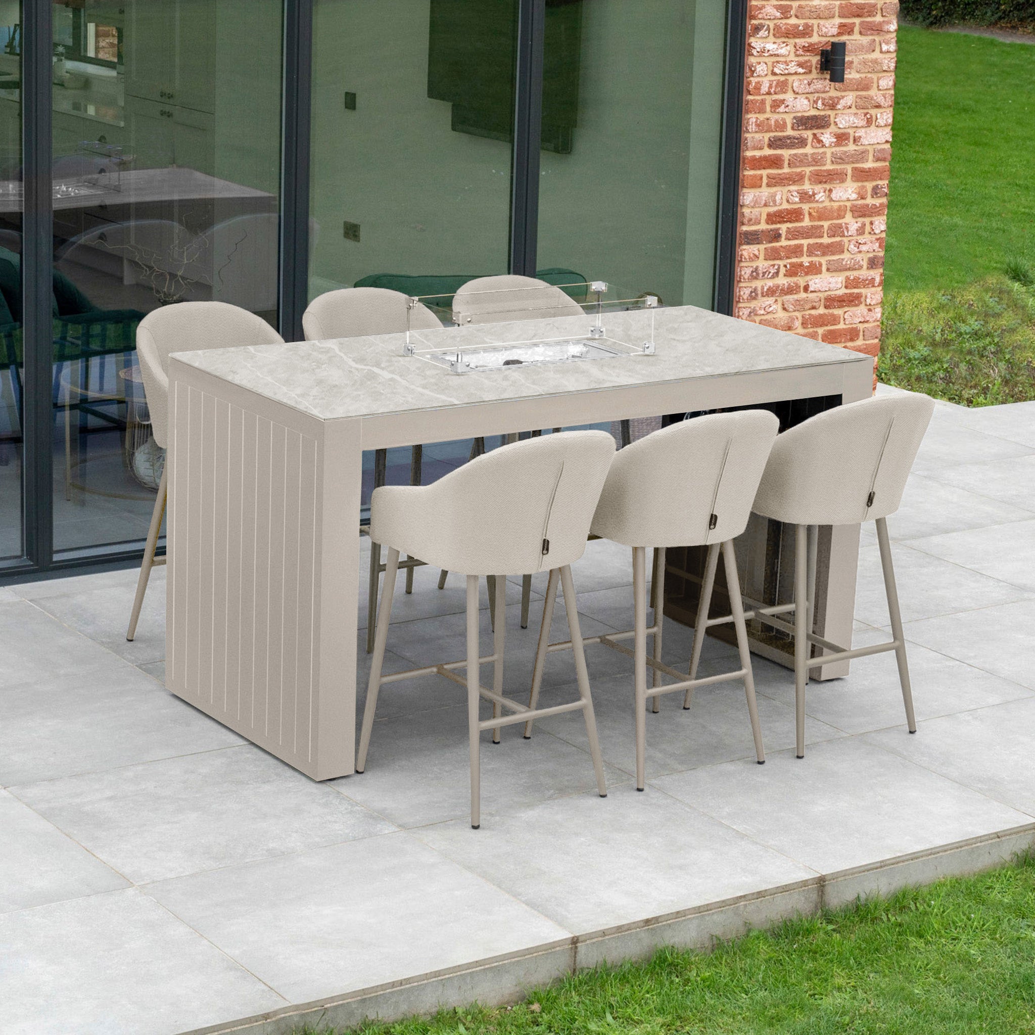 The Luna 6 Seat Outdoor Fabric Ceramic Firepit Bar Set in Fawn showcases six chairs upholstered in beige Luna outdoor fabric, ensuring a stain-proof experience. A light gray rectangular table is gracefully positioned on the patio against a brick wall, fostering an inviting ambiance for gatherings.