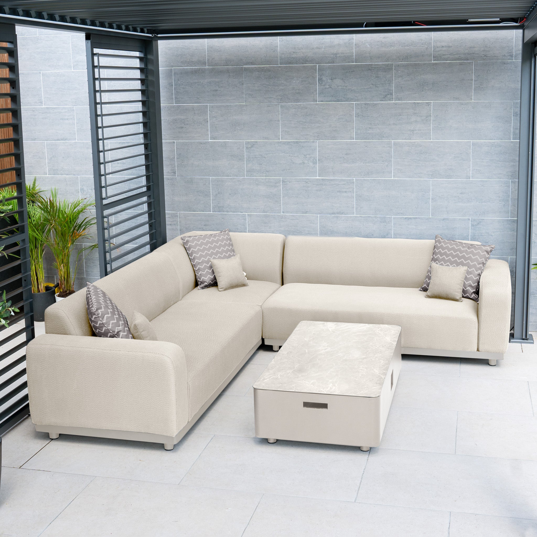 A contemporary outdoor seating arrangement with the Luna Outdoor Fabric Corner Sofa Set in fawn, featuring a durable L-shaped sofa, geometric cushions, and a matching rectangular coffee table. Its design ensures style and low maintenance.