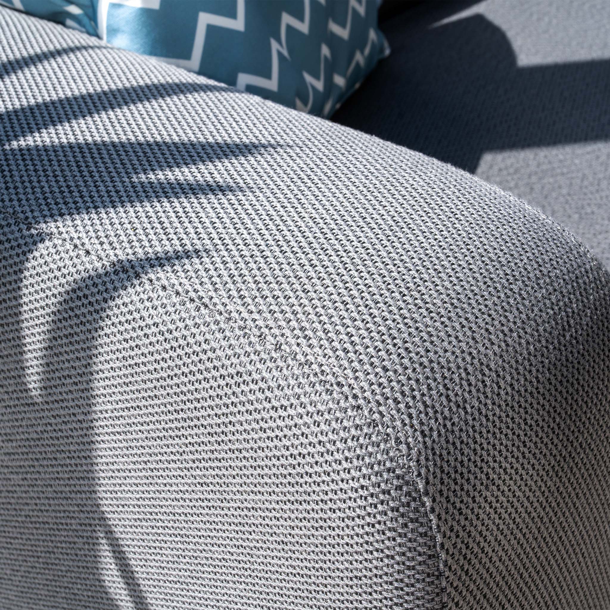 Close-up of the Luna Outdoor Fabric Corner Sofa Set in Grey, featuring a blue and white patterned pillow, illuminated by natural light.