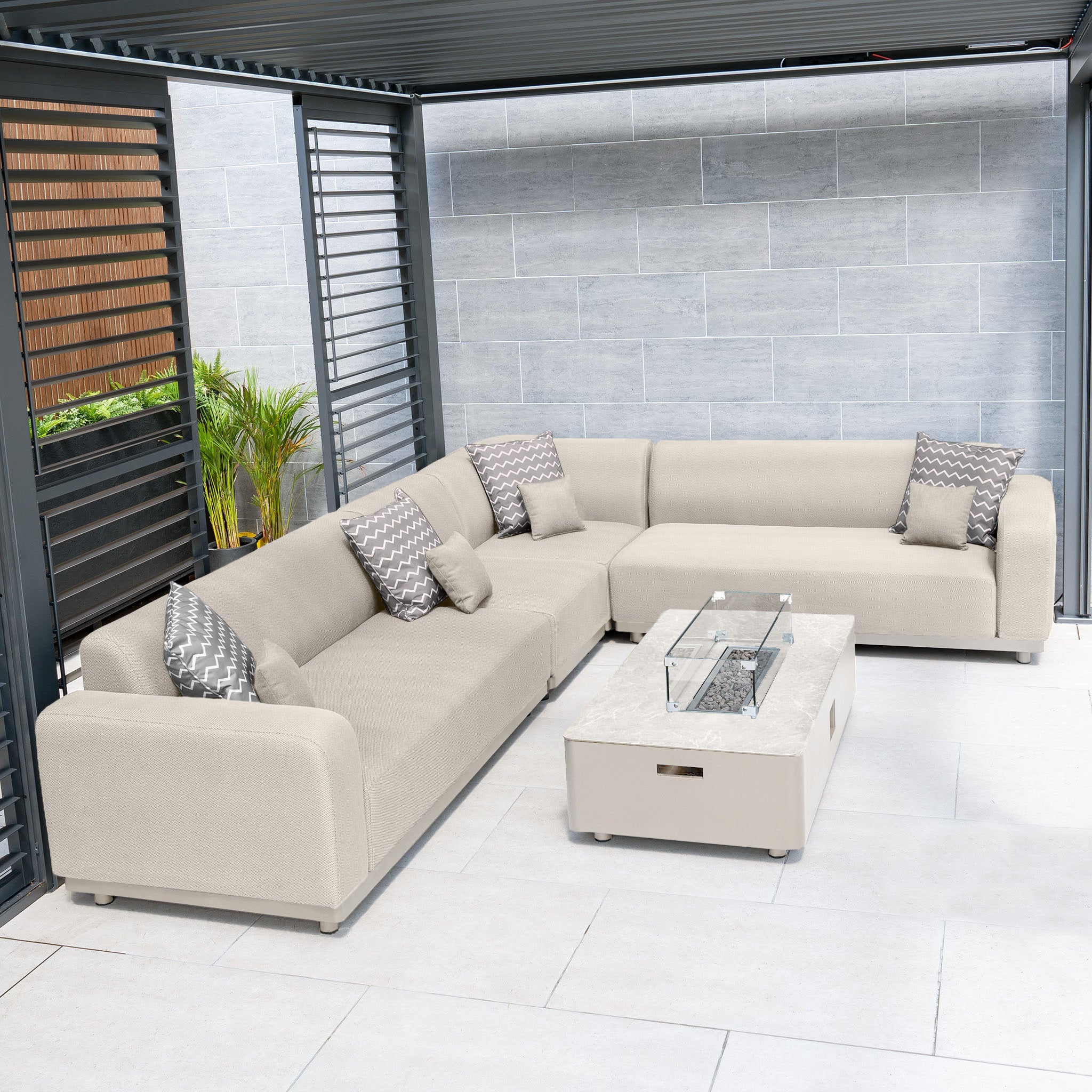 The outdoor seating area showcases the Luna Outdoor Fabric Corner Group Set in Fawn, complete with a firepit coffee table and patterned cushions under the pergola. Experience comfort and style with Harbour Lifestyle Luna's elegant design.