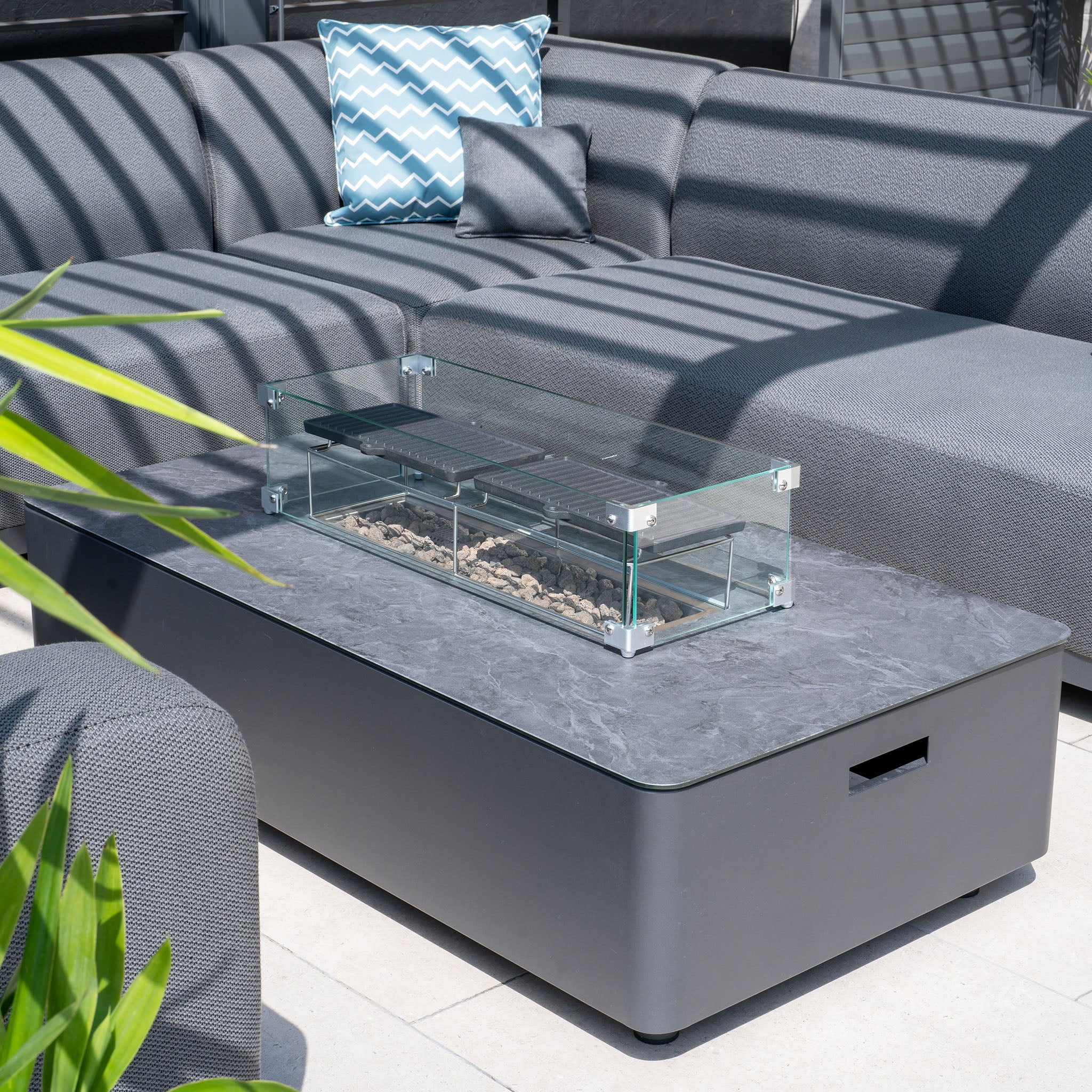 Modern outdoor seating area with the Luna U-Shape Outdoor Fabric Sofa Set with Firepit Coffee Table in Grey, paired with a blue patterned pillow for a sleek and stylish look.