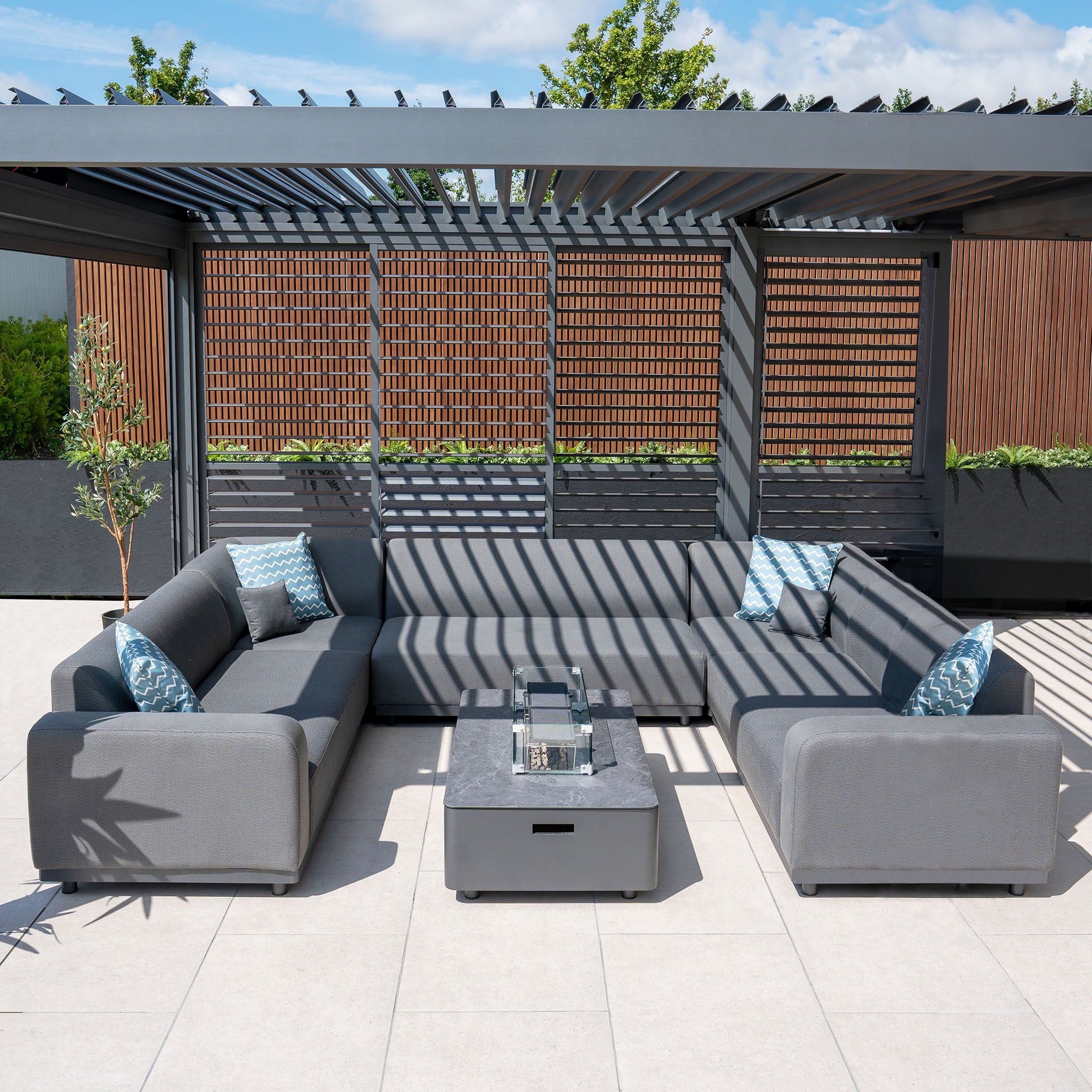 Outdoor patio with a Luna U-Shape Outdoor Fabric Sofa Set with Firepit Coffee Table in Grey featuring geometric patterned cushions and a pergola with lattice walls.