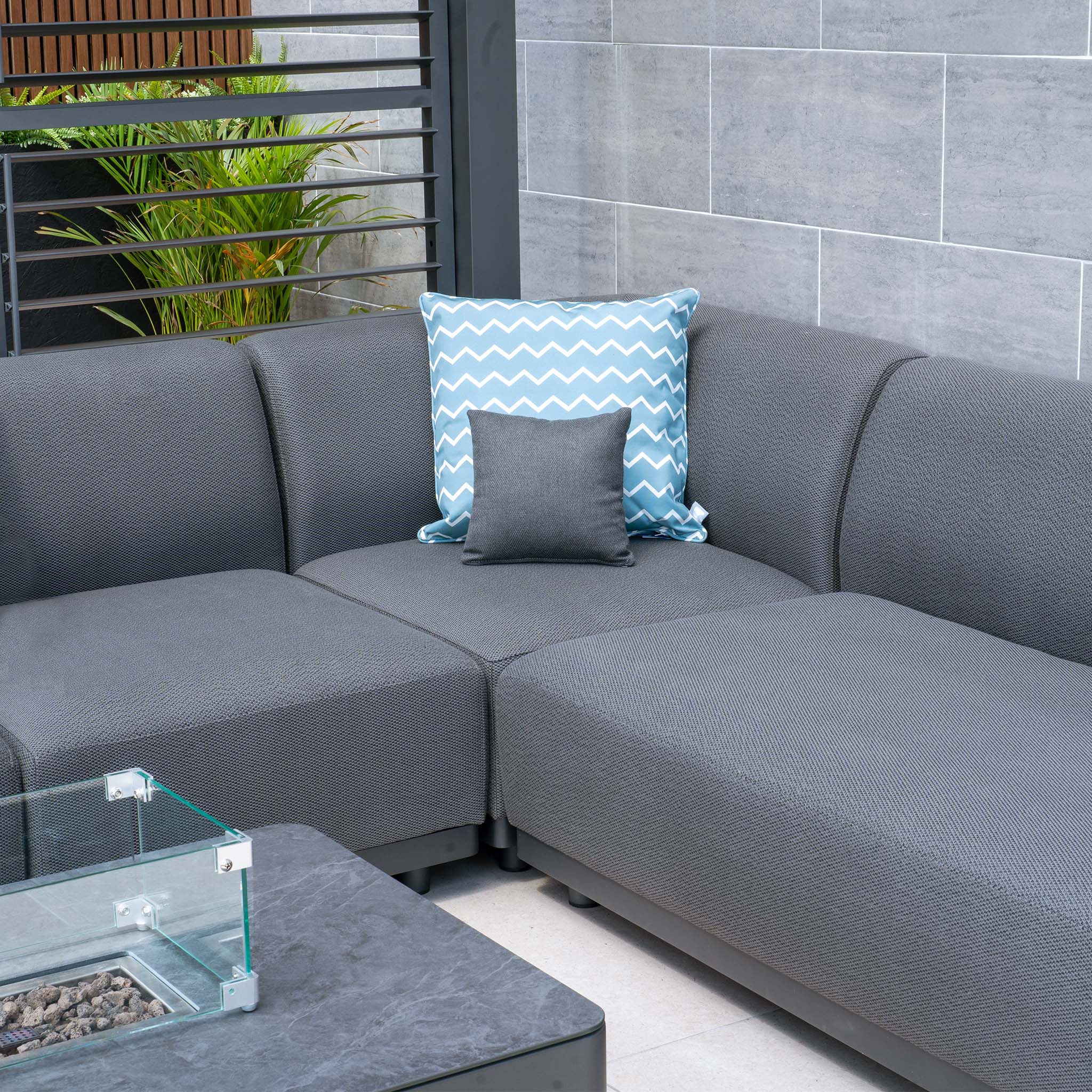 The Luna U-Shape Outdoor Fabric Sofa Set with a Firepit Coffee Table in Grey includes two decorative pillows, one featuring a blue chevron pattern.