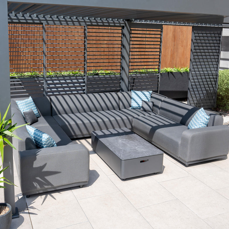 Contemporary outdoor patio featuring the Luna U-Shape Outdoor Fabric Sofa Set in Grey with blue patterned cushions, a matching coffee table, and a slatted wooden screen overhead. This maintenance-free setup guarantees lasting comfort and style.