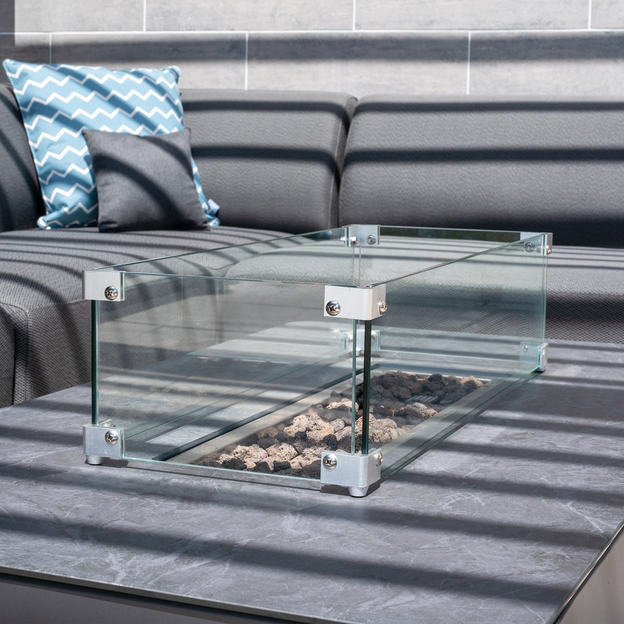 A Ceramic Firepit Coffee Table in Grey, featuring a glass rectangular fire pit with stones inside, set on an aluminium frame and finished with TIGER Drylac® Powder Coating.