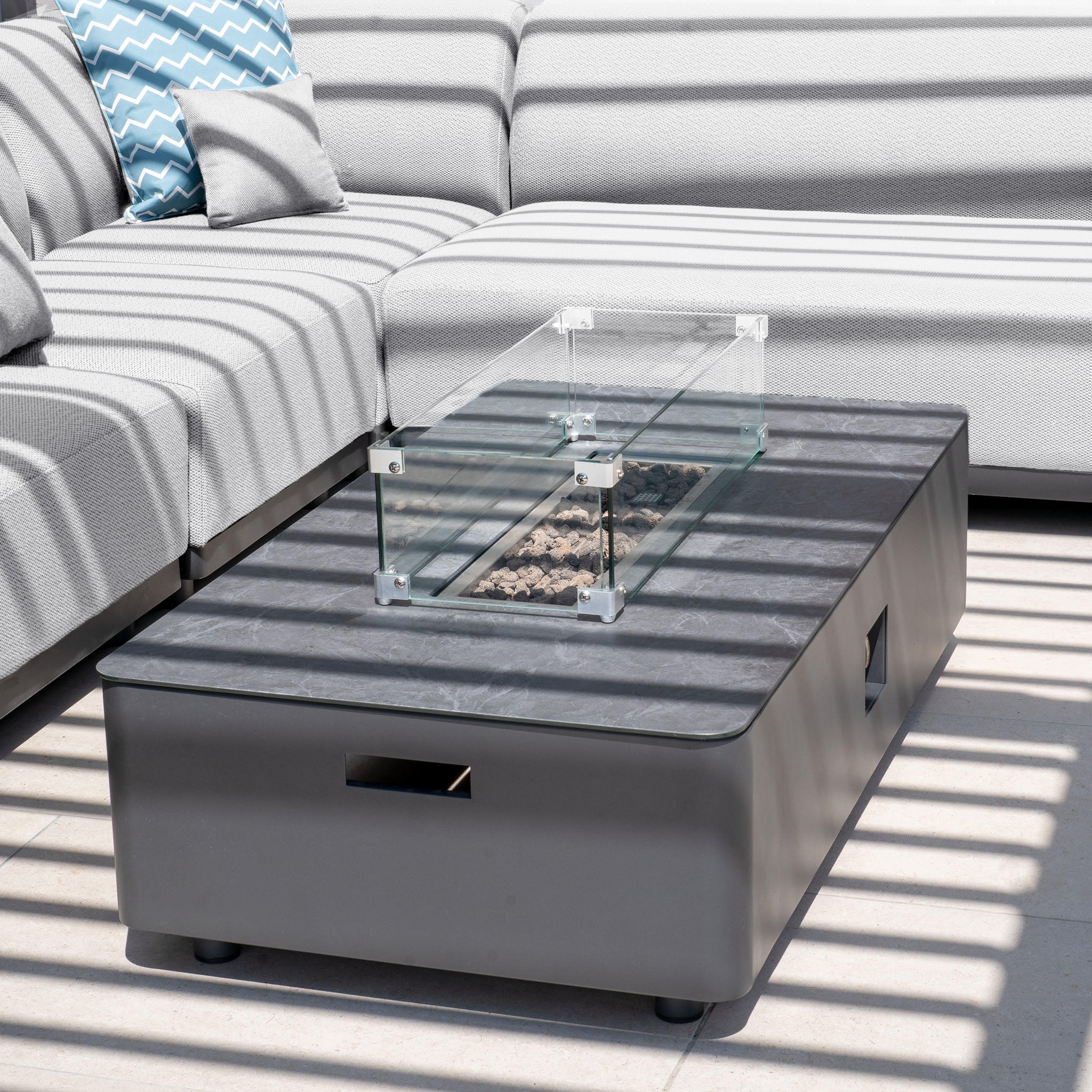 Elevate your patio with the Luna Outdoor Fabric Corner Sofa Set in Oyster Grey, complete with a sleek firepit coffee table. Experience Harbour Lifestyle's blend of comfort and style under beautifully cast striped shadows.